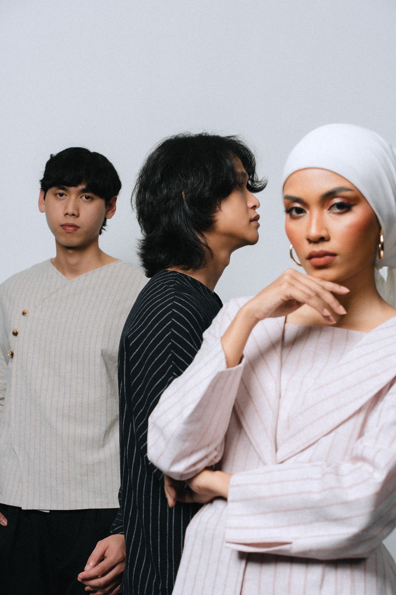 Three young Asian models pose against a white background, woman in hijab foreground, two men behind her.