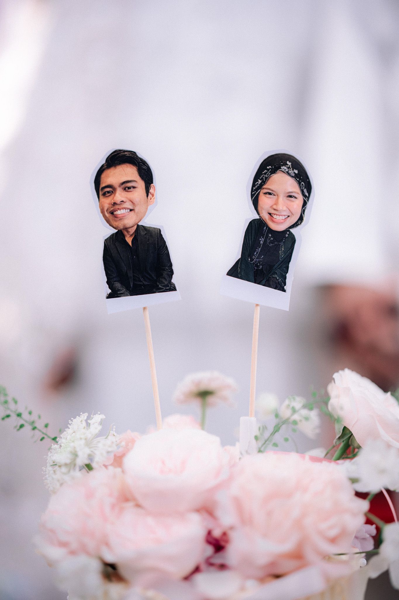 Custom caricature cake toppers of a couple in black outfits displayed above pink and white floral arrangement.