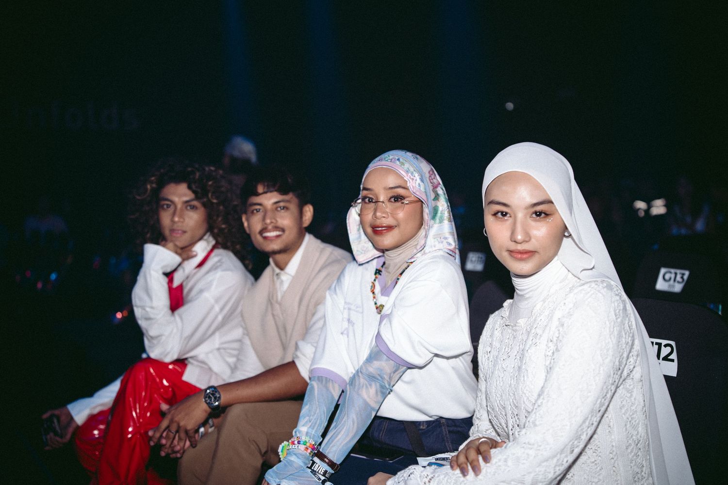 Four people sit together at a nighttime event wearing traditional modest clothing and hijabs.