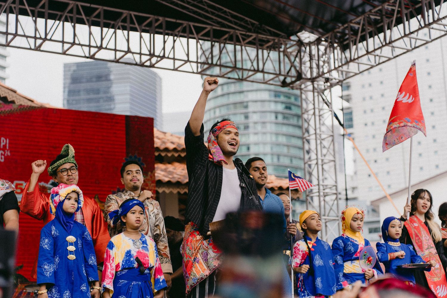 Group performance on stage with colorful outfits and raised arms during a daytime event.