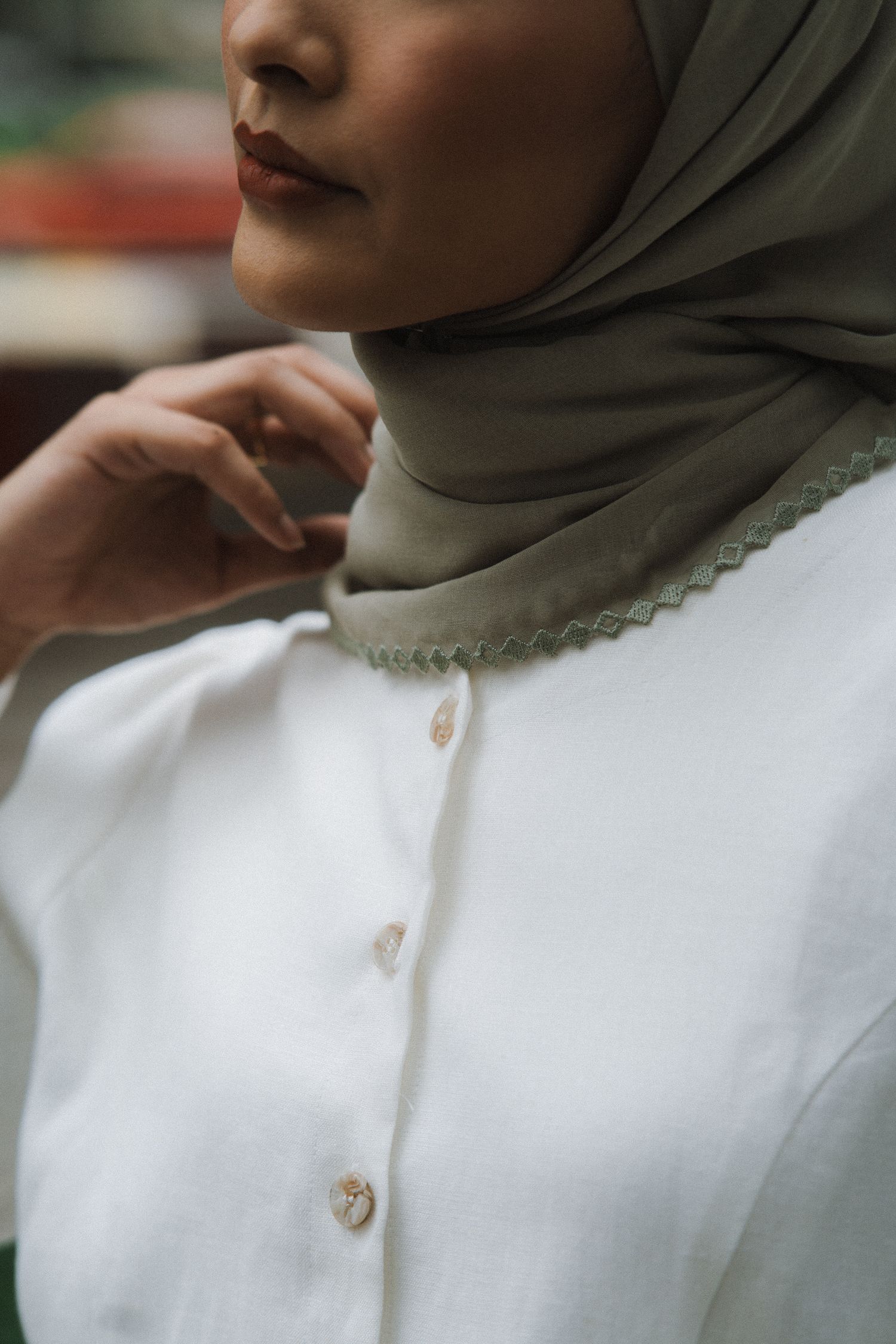 Close-up shot of a hijab in muted olive color paired with white buttoned clothing.