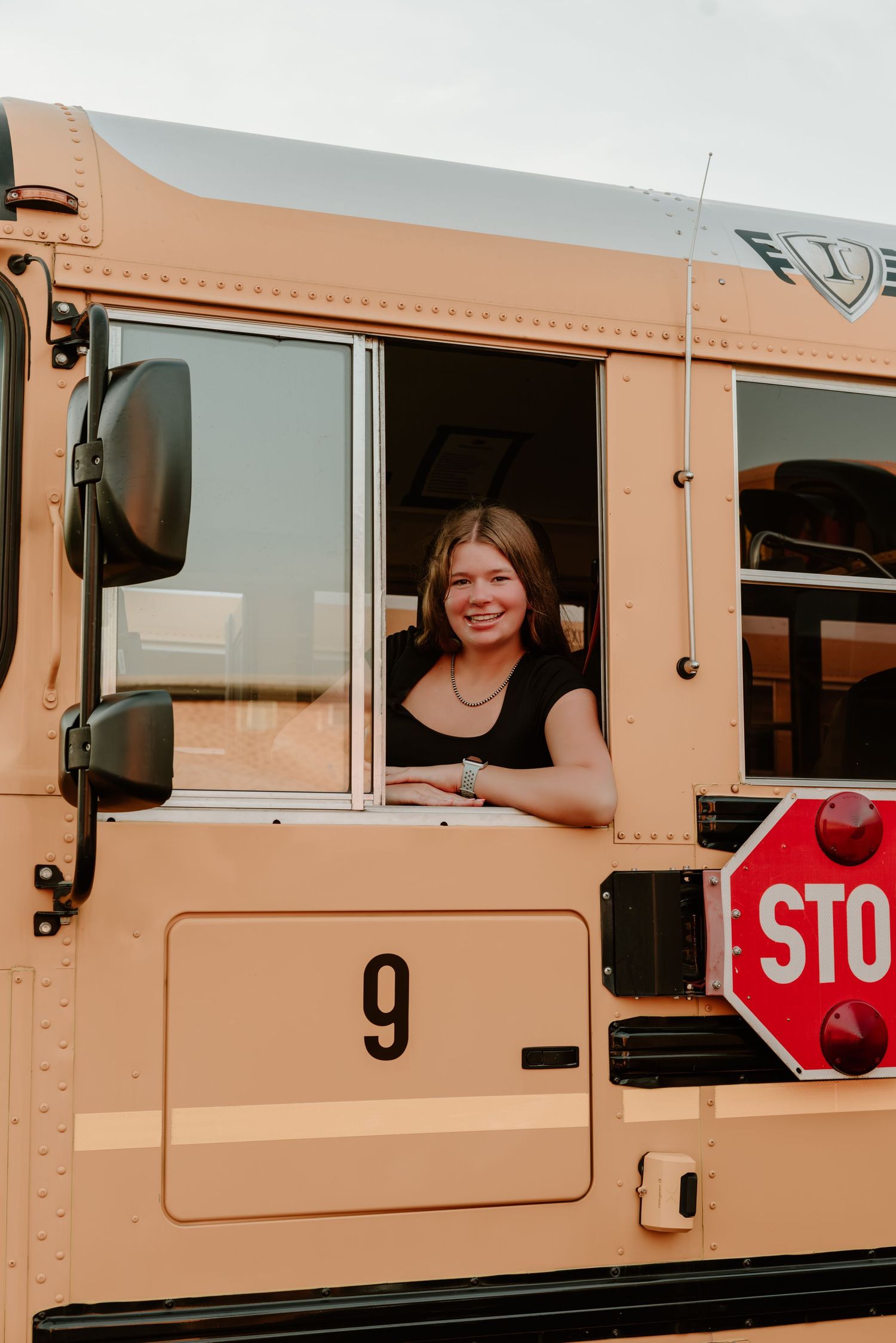 Student smiles through the driver's window of school bus number 9.