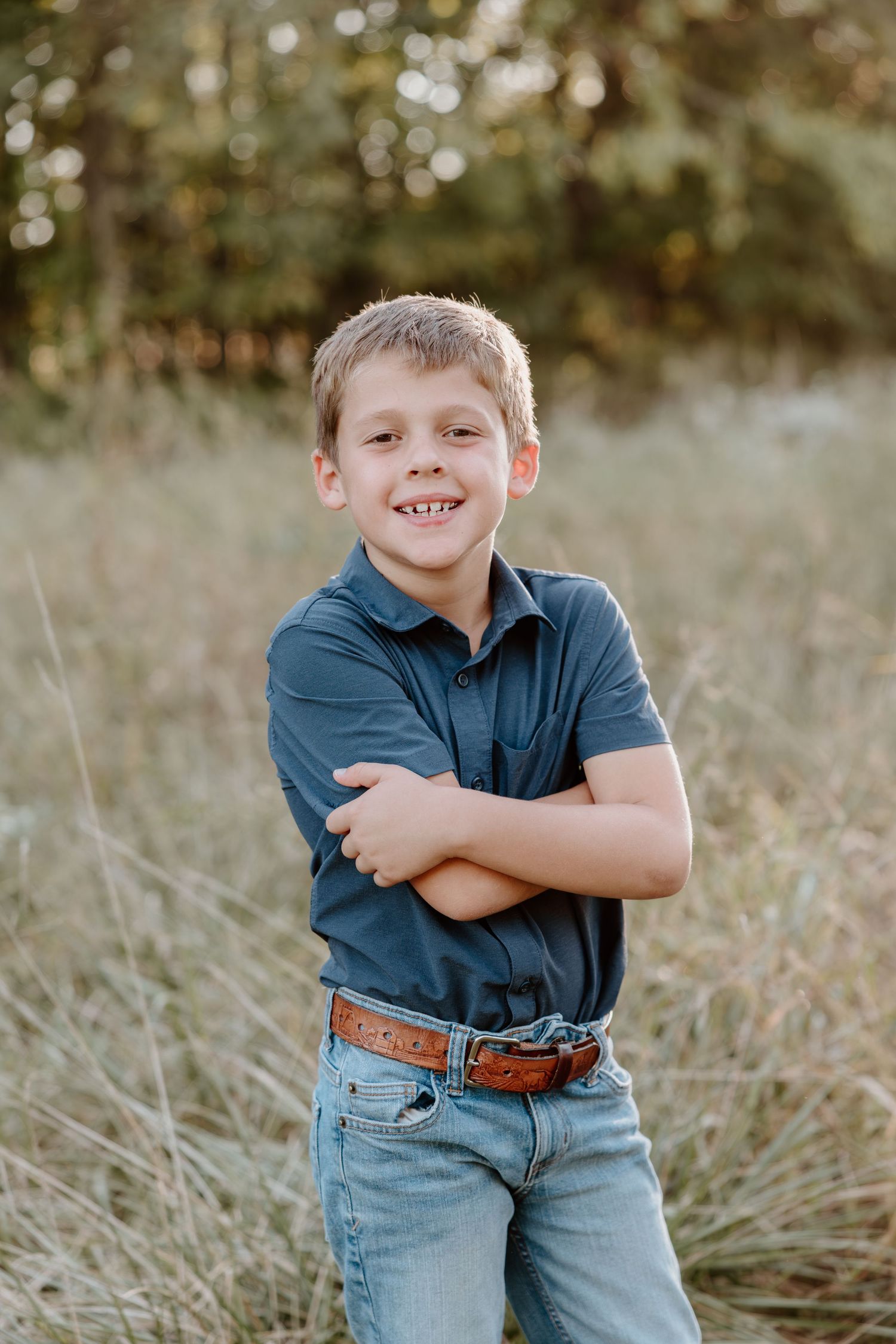 A child in a navy blue shirt and jeans poses outdoors in a grassy field with natural lighting.