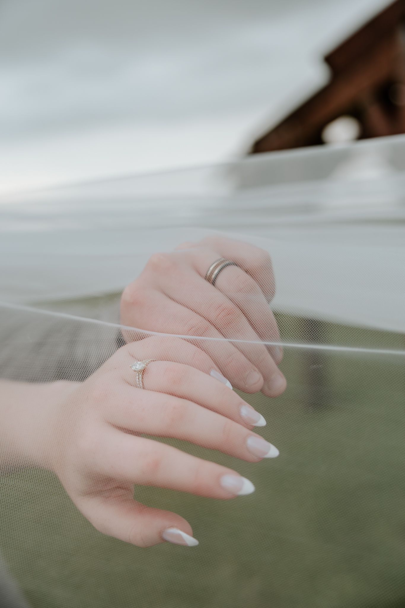 Close-up of bride and grooms hands wearing wedding rings with elegant white manicured nails.