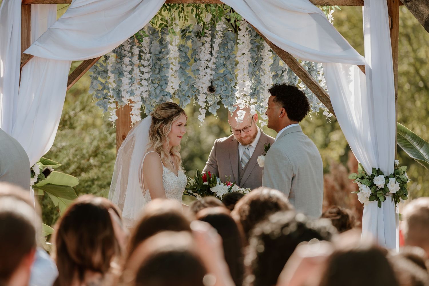 Bride and groom exchange vows under floral arch at outdoor wedding ceremony.