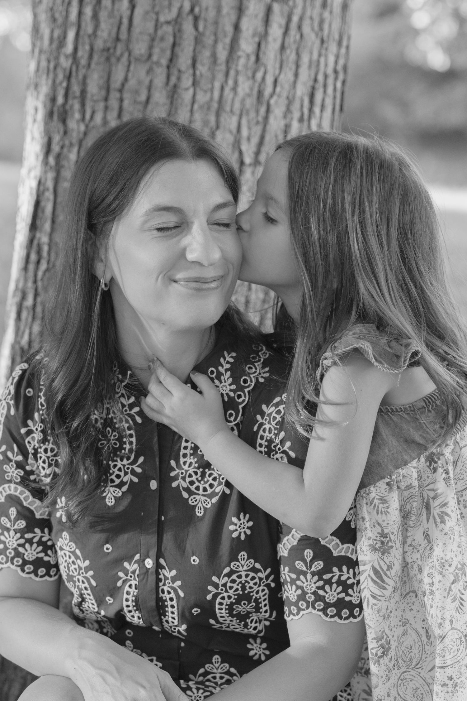 Black and white photo series showing tender moments between two people leaning against a tree trunk.