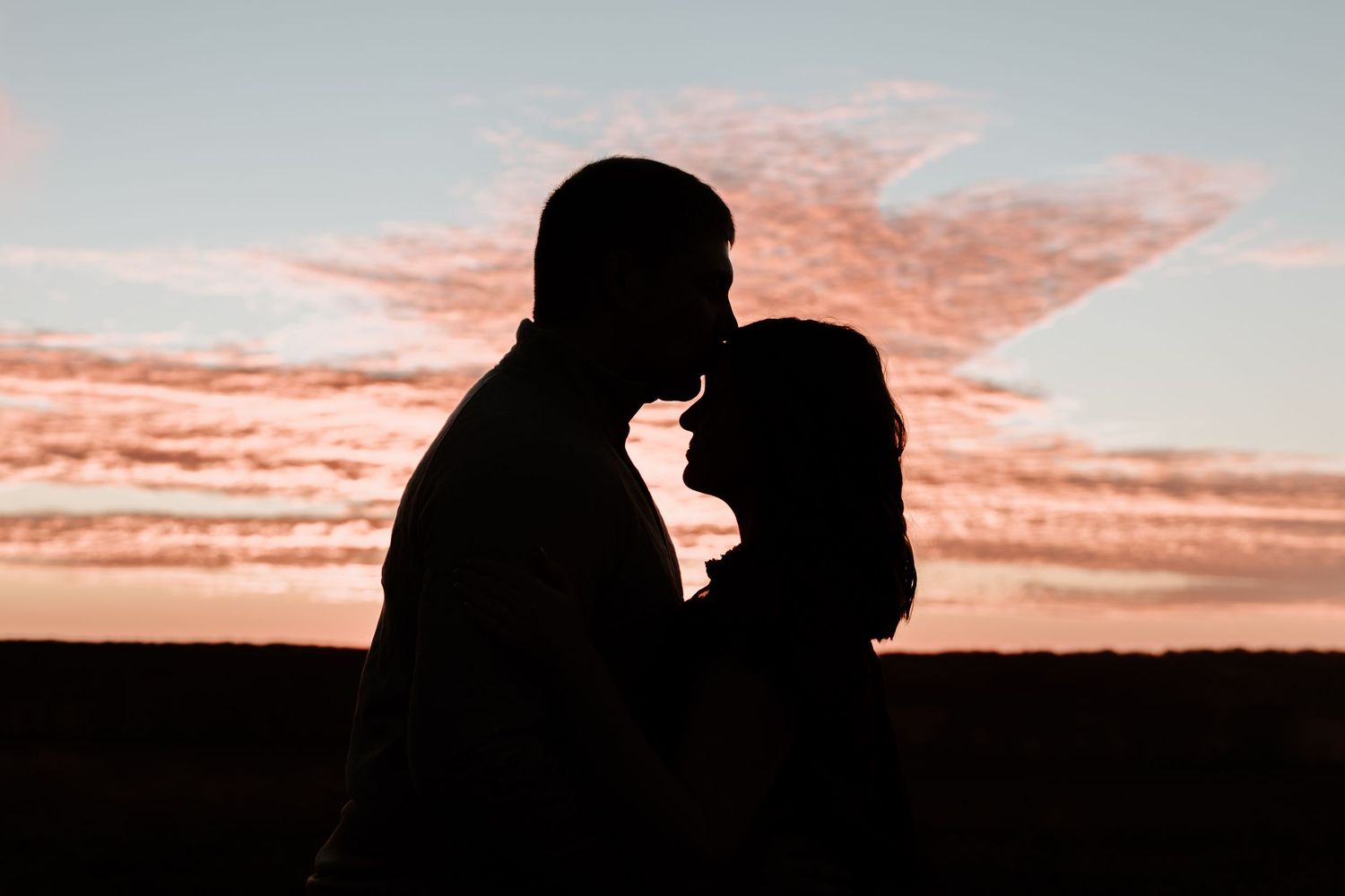 Silhouettes of two people kissing against a dramatic orange and pink sunset sky.