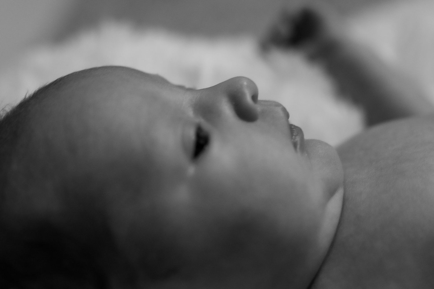 Black and white close-up profile view of a sleeping baby laying on soft bedding.