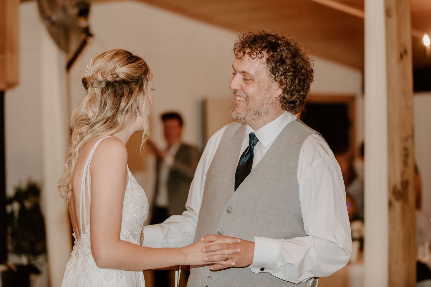 Bride and father sharing a tender moment together during wedding ceremony in rustic barn.