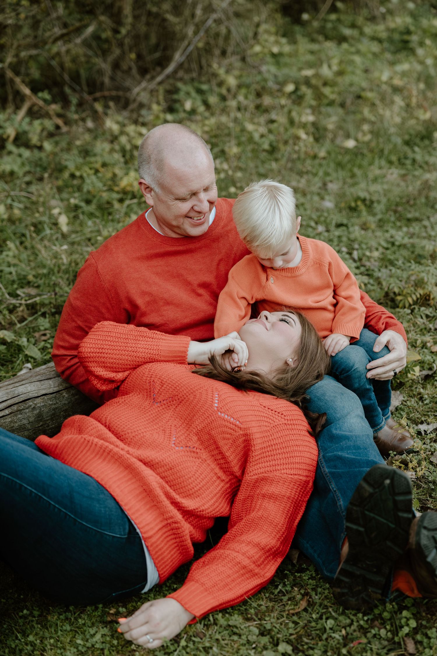 A series of candid outdoor photos showing tender moments between two people wearing matching orange sweaters on grass.
