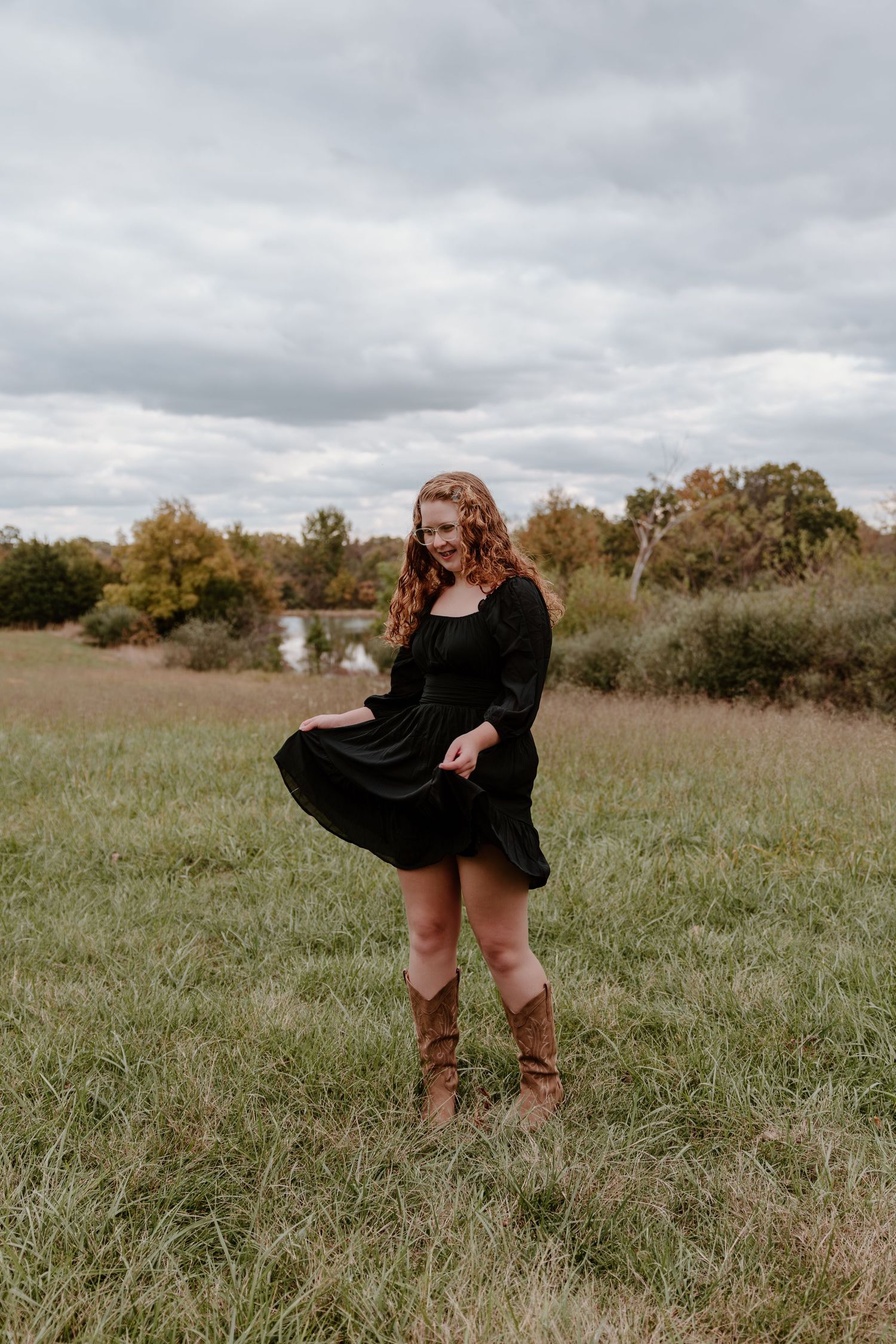 A person in a black dress twirls playfully in a grassy autumn field under cloudy skies.