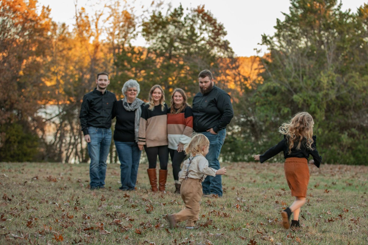 Candid family photo with children running and playing in a fall field at sunset.