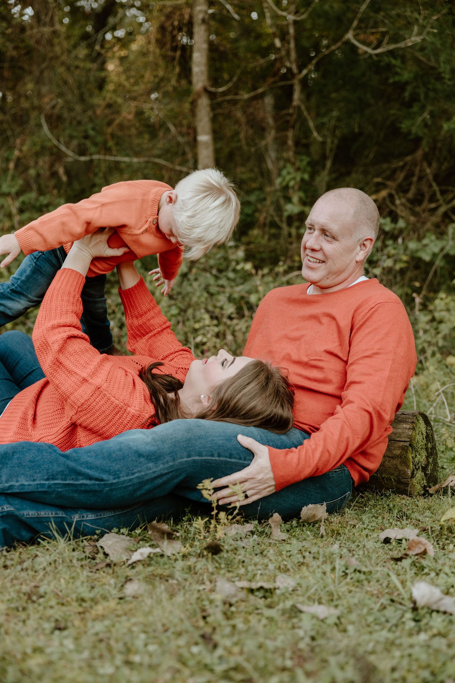 Two people in matching coral sweaters lay together on grass in a romantic outdoor photo session.