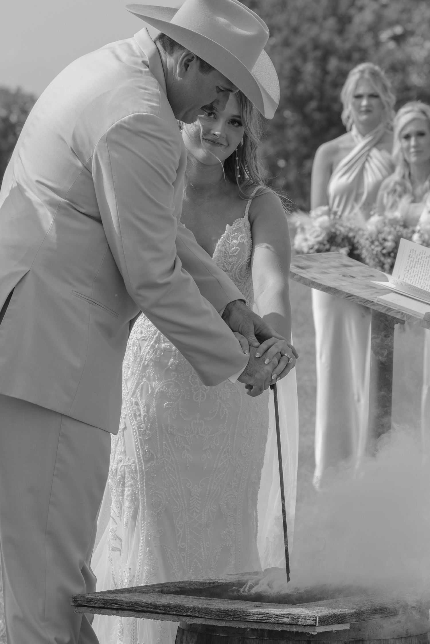 Black and white photo of bride and groom in cowboy hat performing a unity ceremony at outdoor wedding.