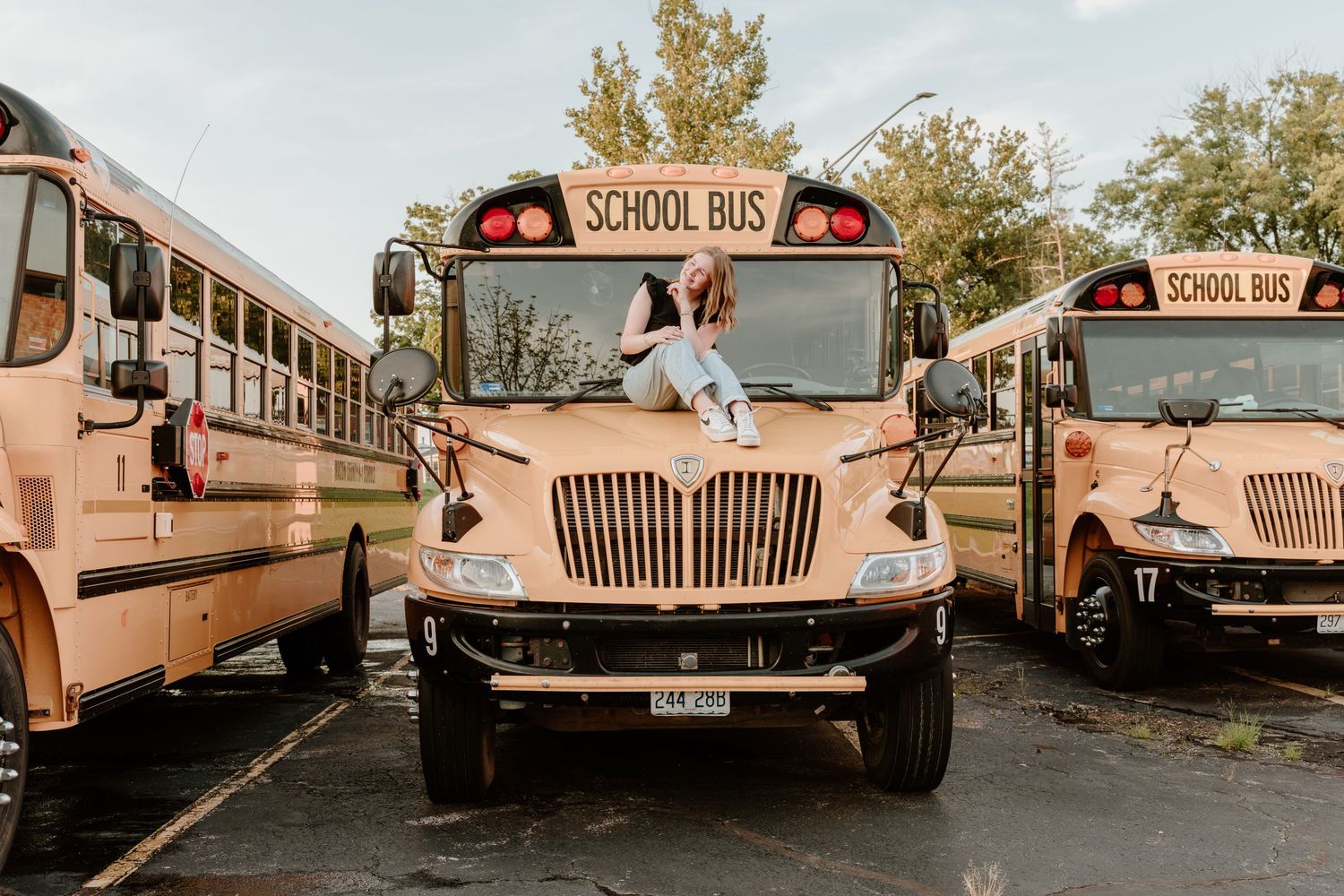 Series of tan vintage school buses parked in a row at an outdoor location during autumn.