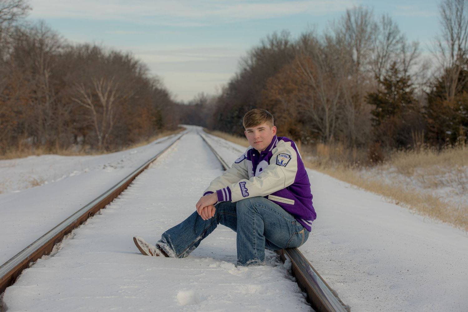 Person sitting on snow-covered railroad tracks in winter.
