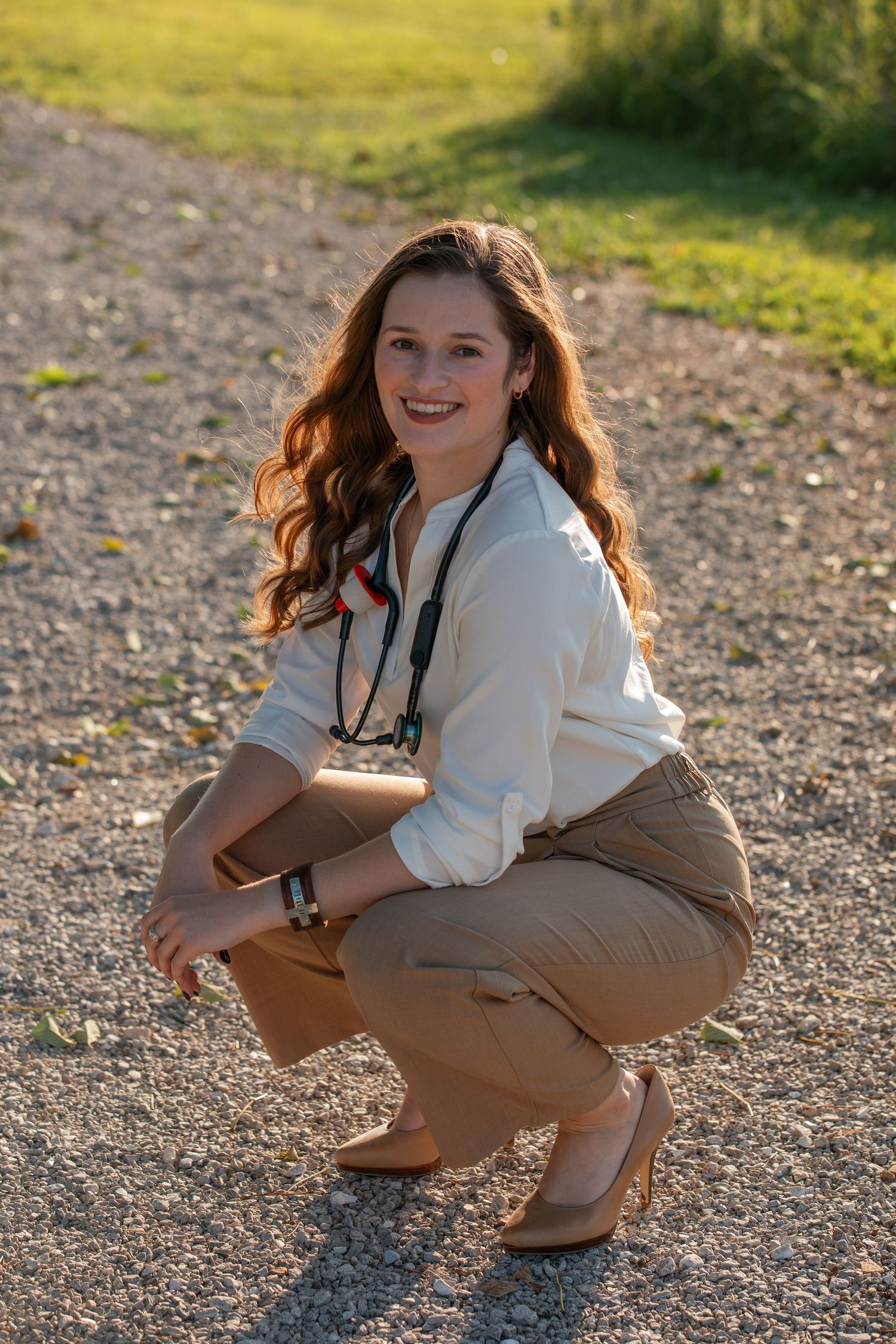 Medical professional in business casual attire crouching outdoors.