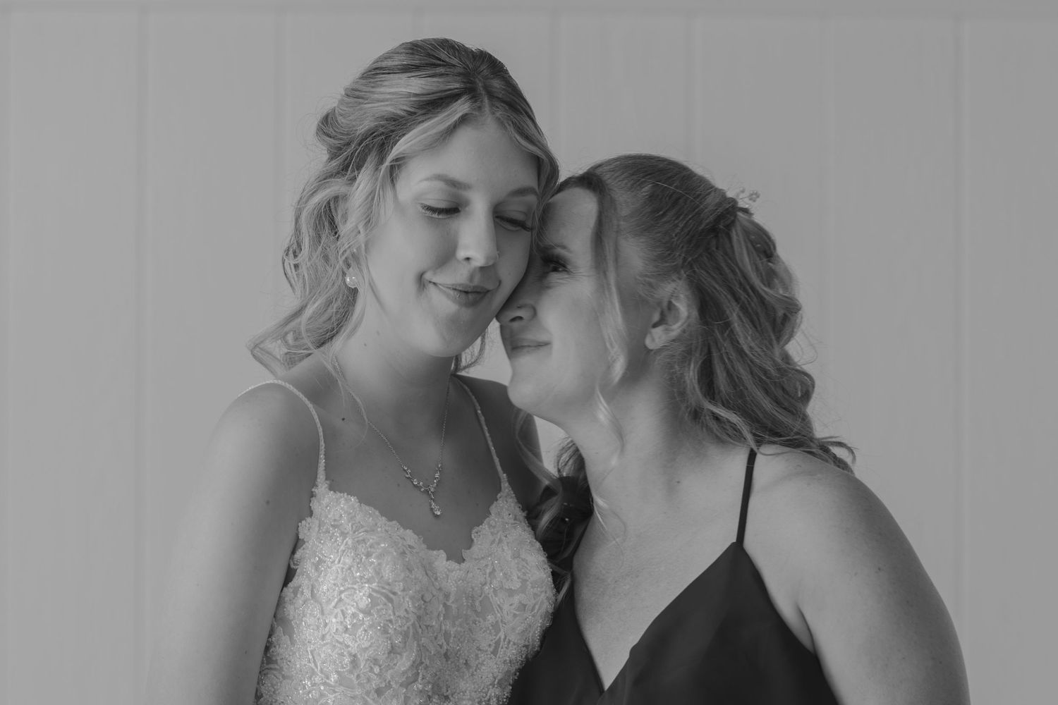 Black and white photo of two bridesmaids sharing a tender moment, smiling together.