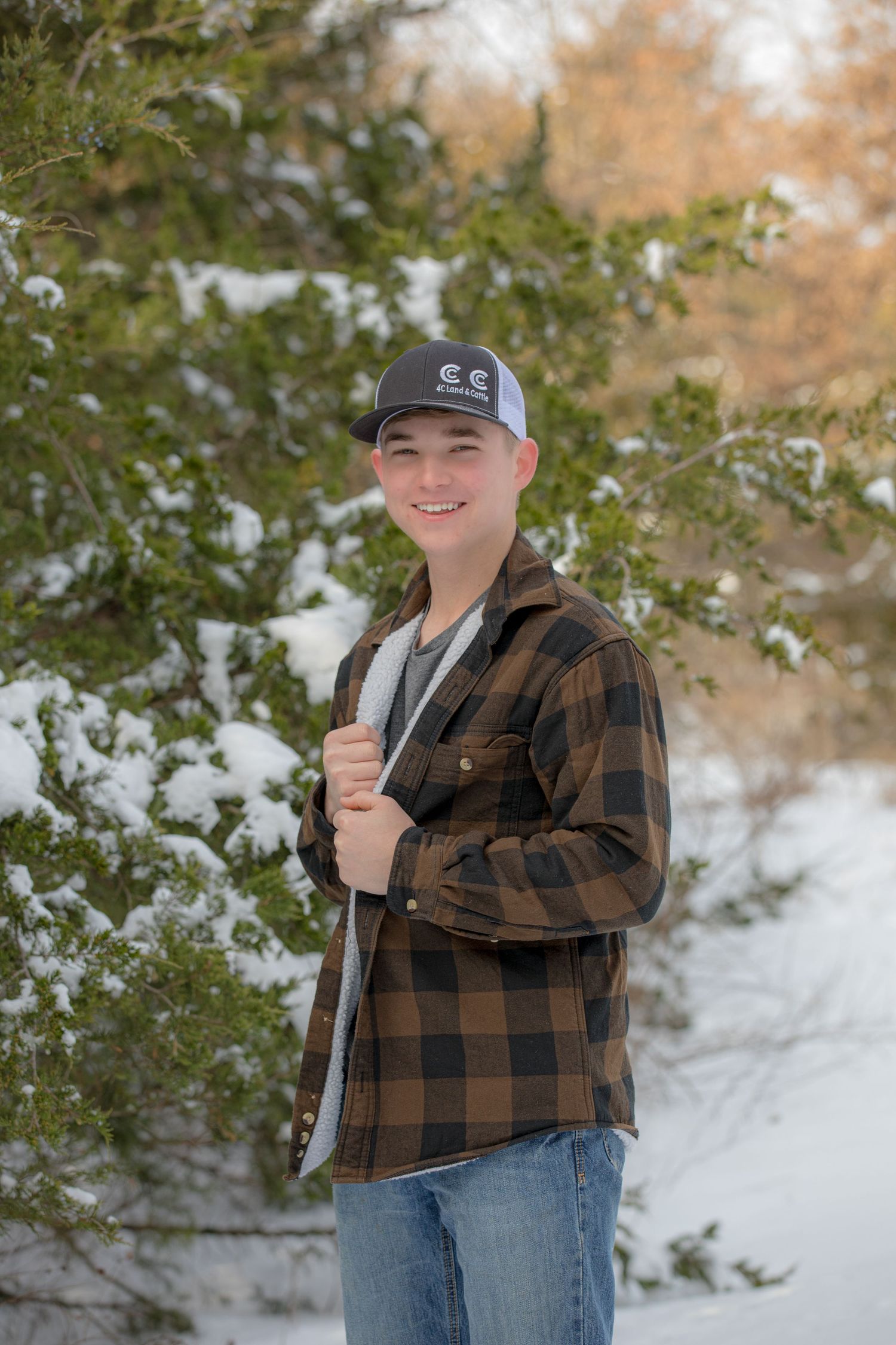 Young person in plaid flannel jacket and baseball cap poses against snowy winter background.