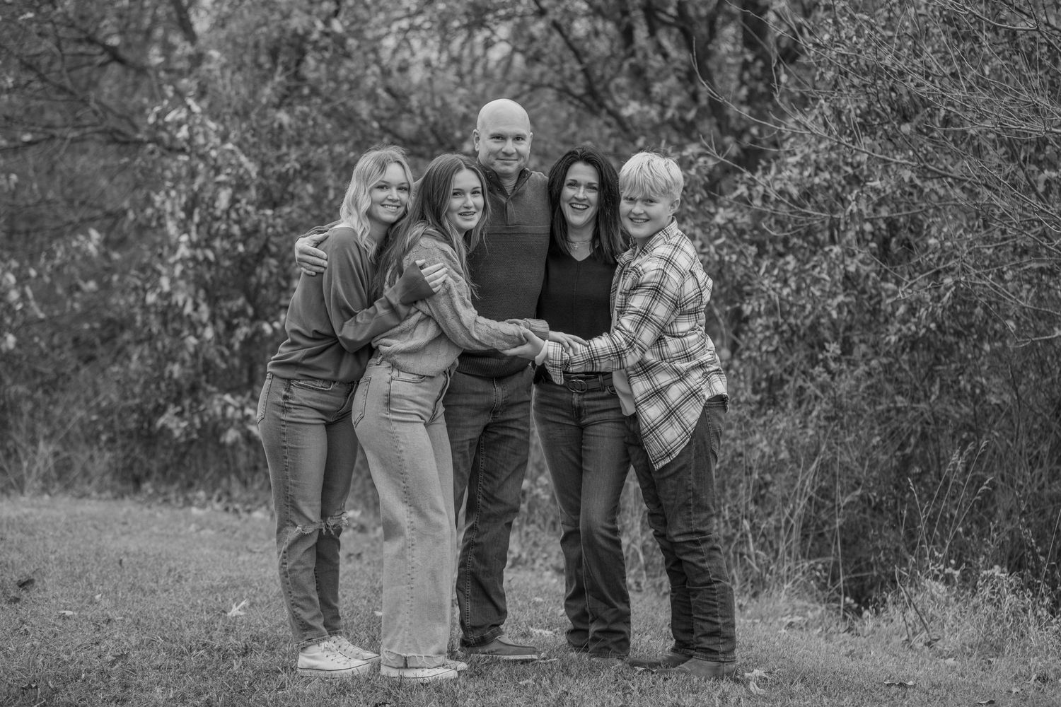 Black and white portrait of family members hugging and smiling together outdoors.