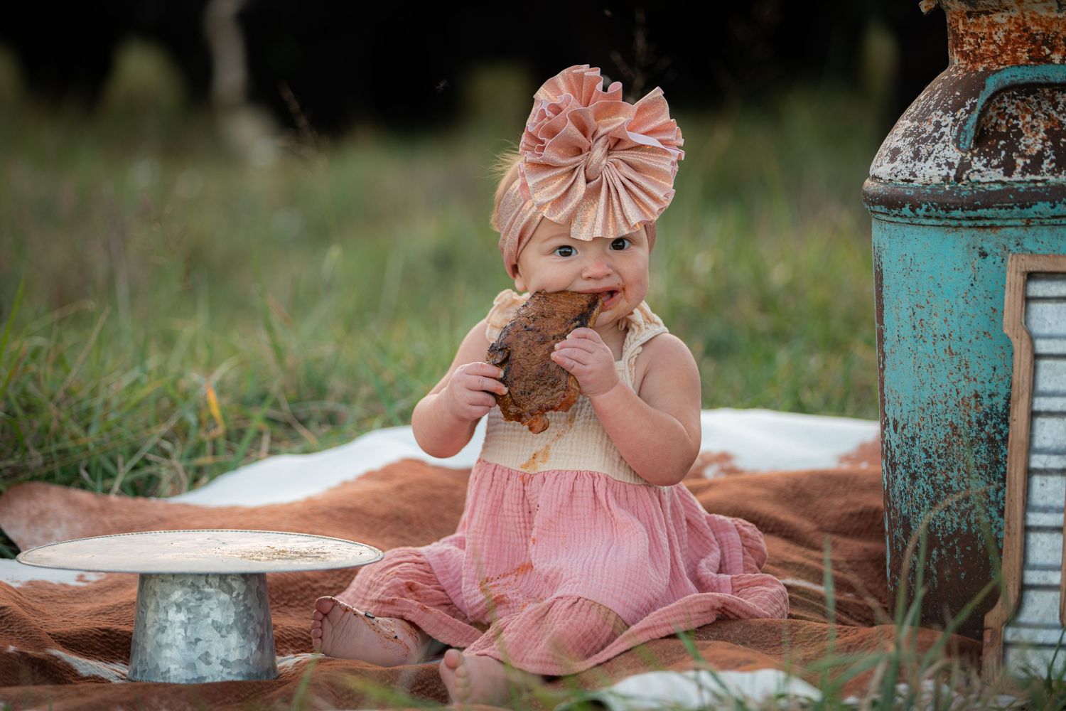 Baby in pink dress having a snack during outdoor photoshoot with vintage props.