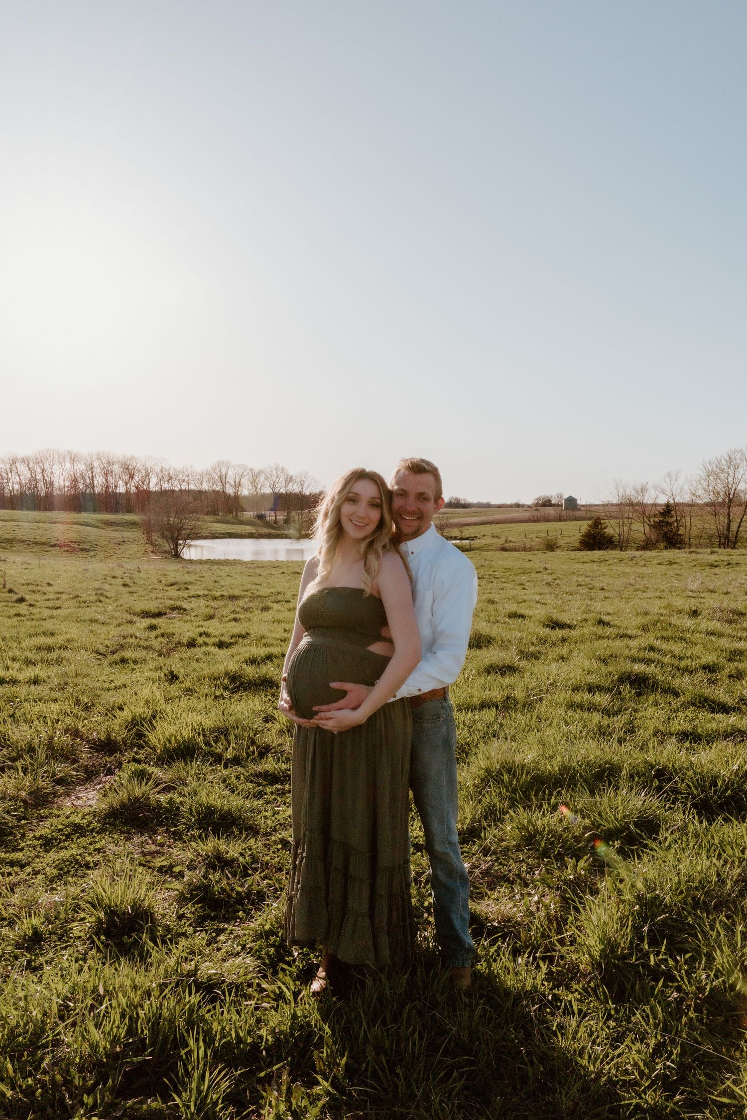 A romantic maternity photo of couple embracing in a sunlit meadow during golden hour.