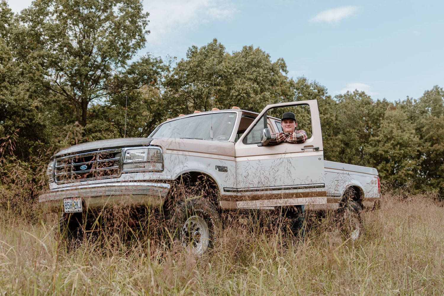 A lifted white Ford Bronco parked in a grassy field on a sunny day with trees in the background.