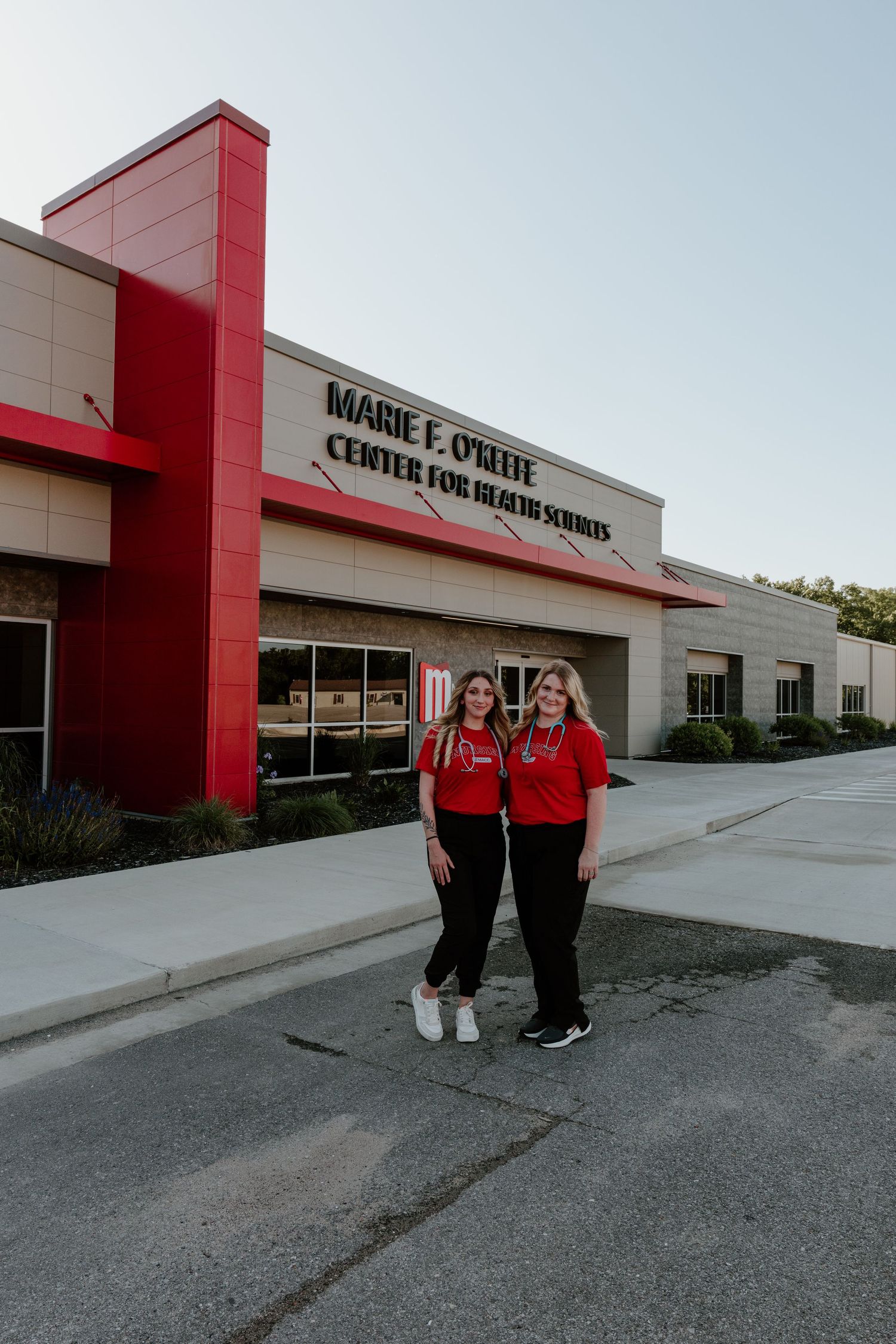 Red and beige stone commercial building with signage and two people in red shirts standing outside.