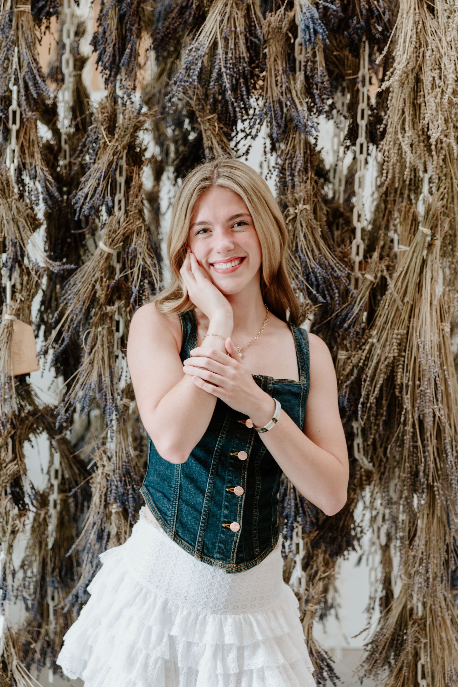 Four photos showing someone wearing a denim top with white dress against a backdrop of dried palm fronds or grass.