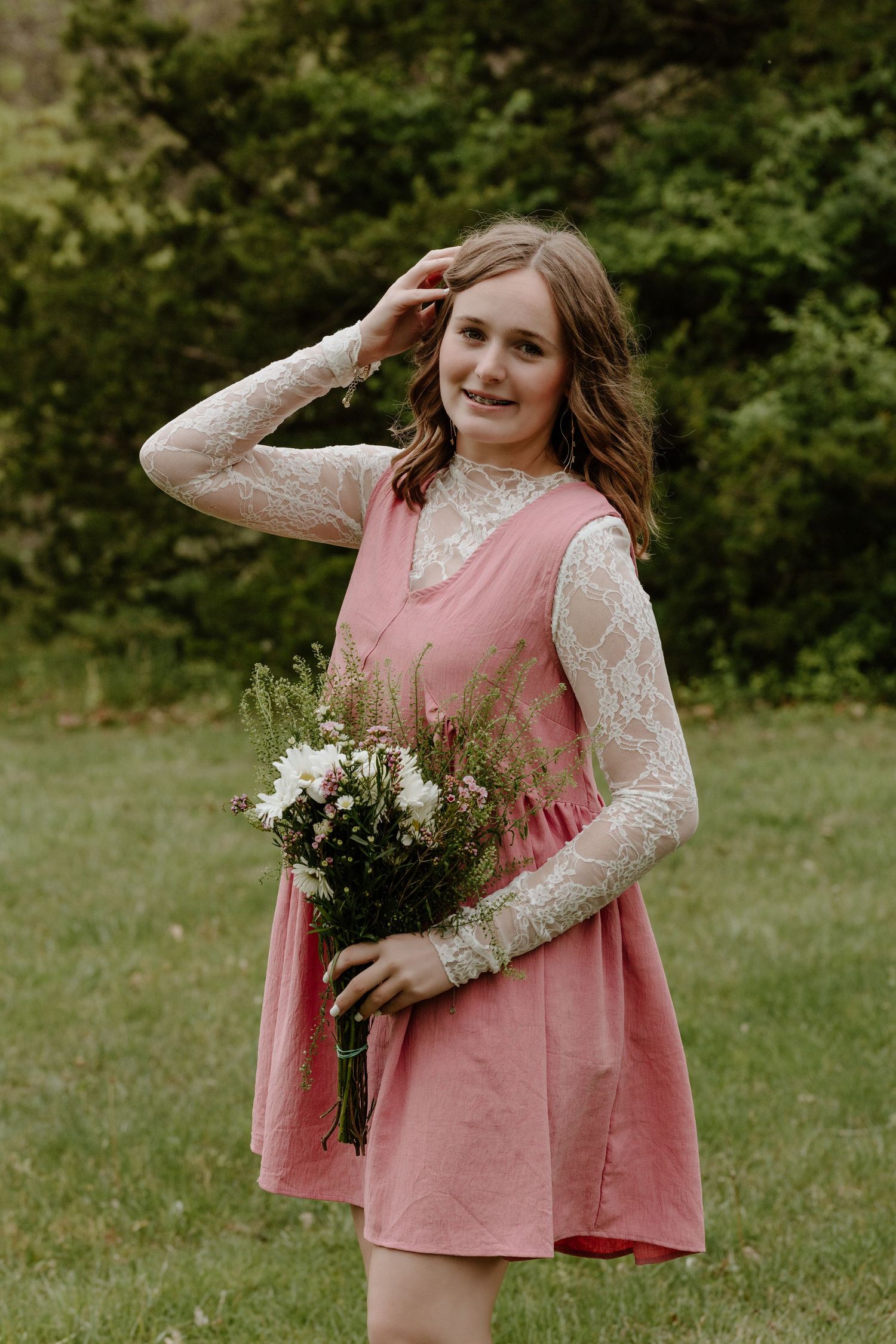 A person in a pink corduroy dress and lace sleeves holds a bouquet of white flowers in an outdoor setting.