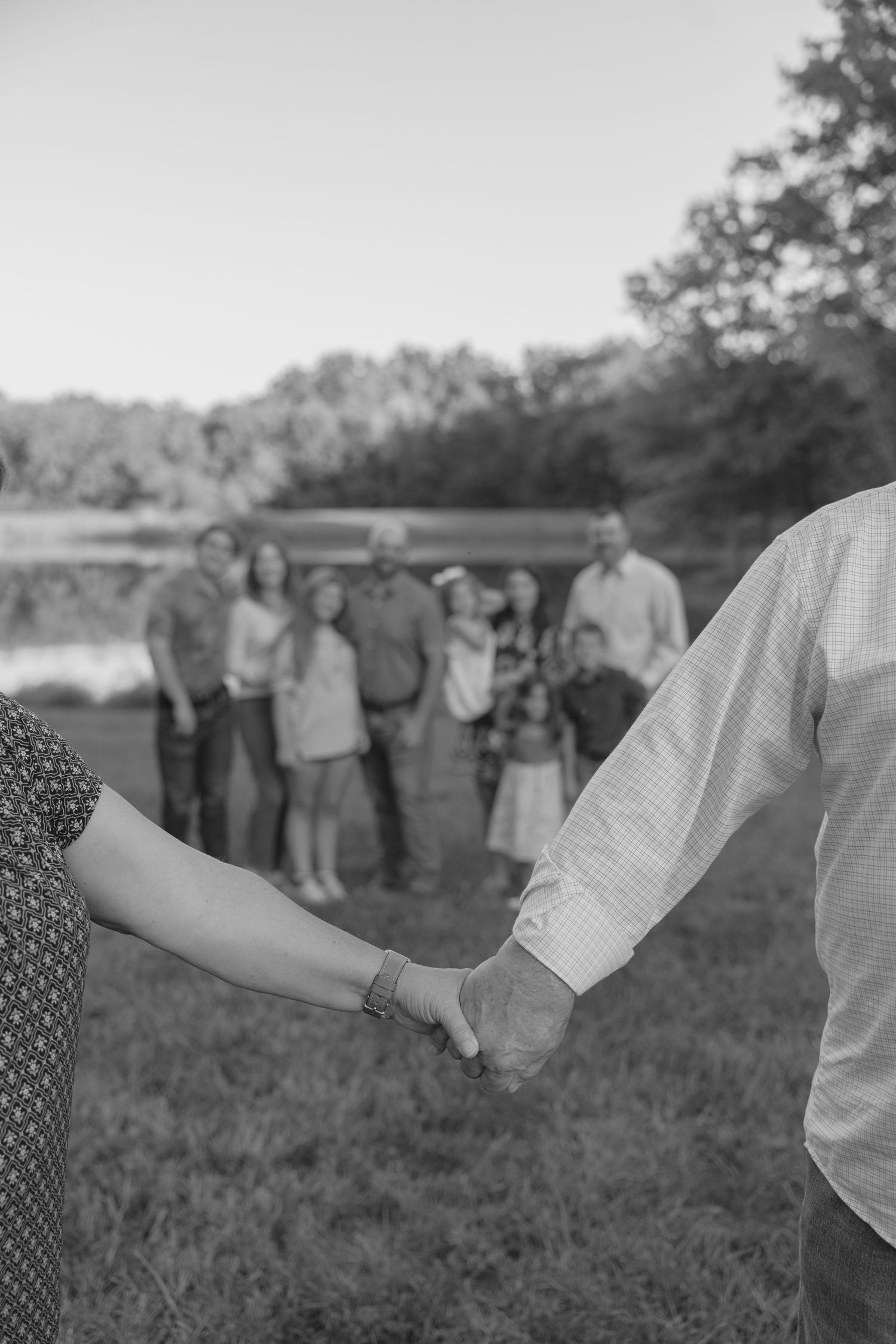 A black and white photograph shows a line of people holding hands in a field during what appears to be a folk dance.