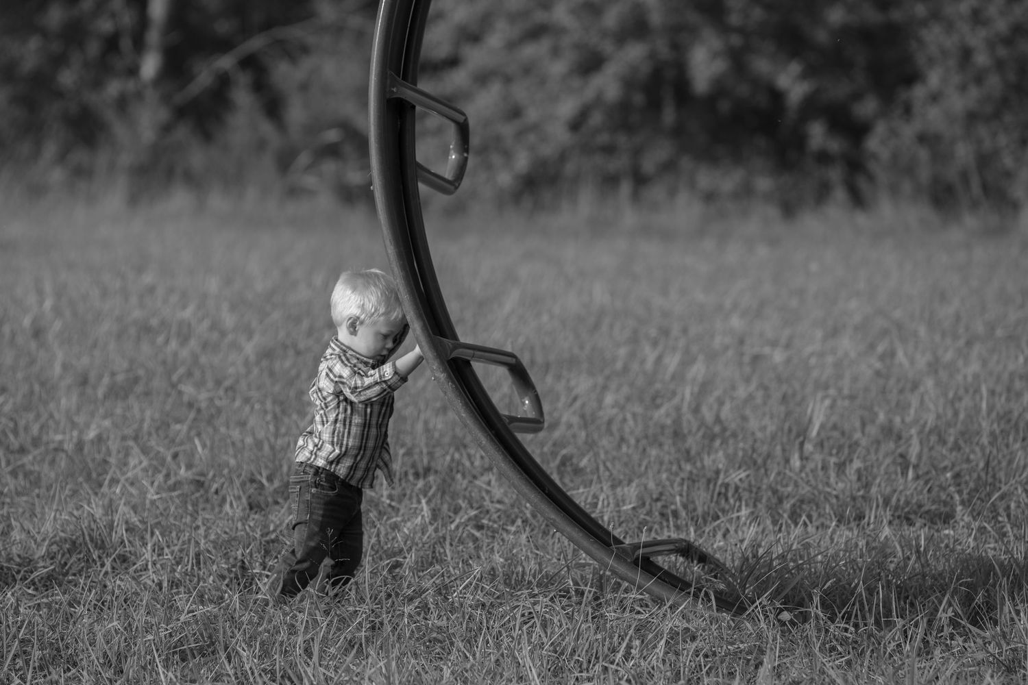Black and white image of small child playing on curved playground equipment.