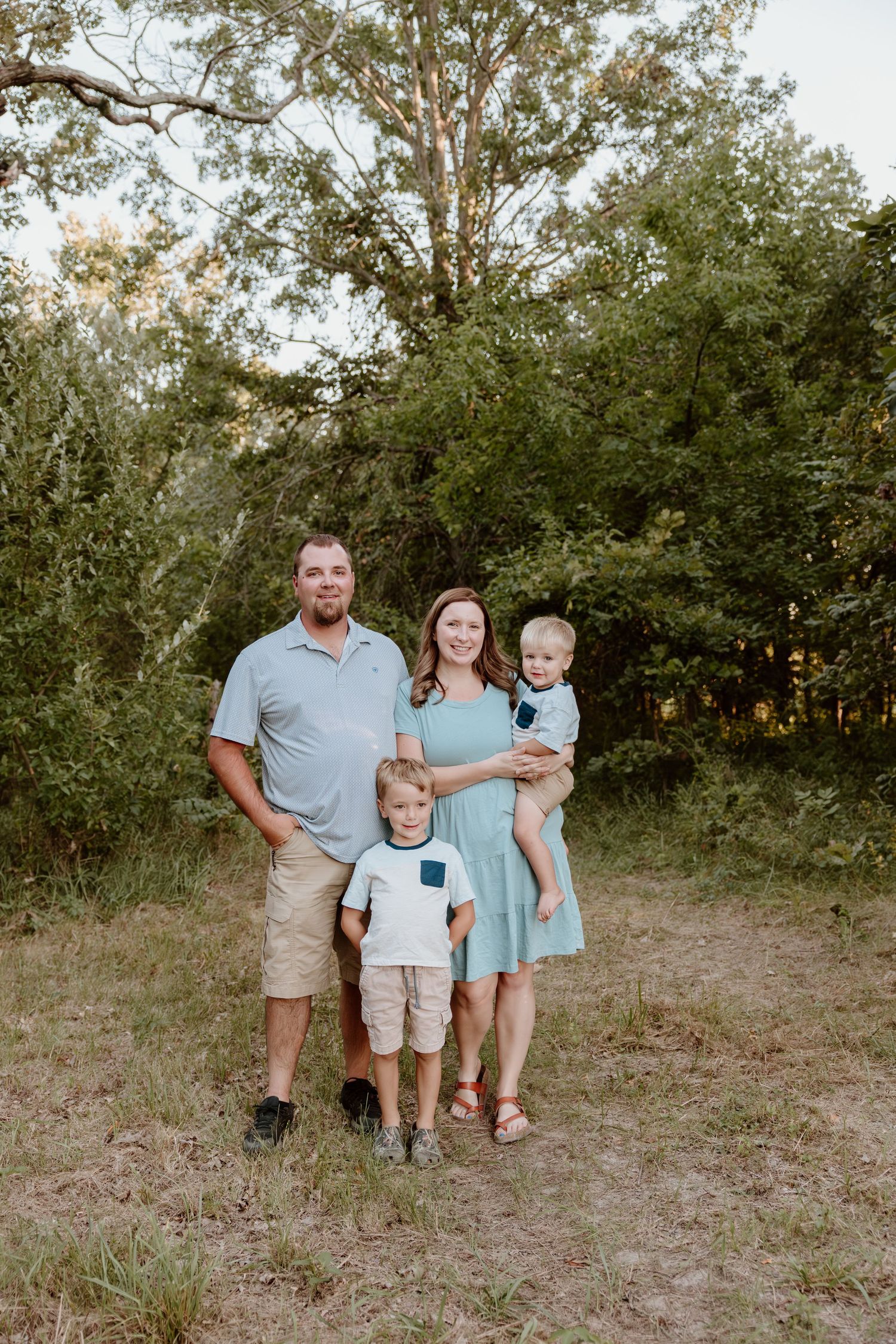 Family enjoying a casual outdoor photo session in a natural wooded setting at sunset.