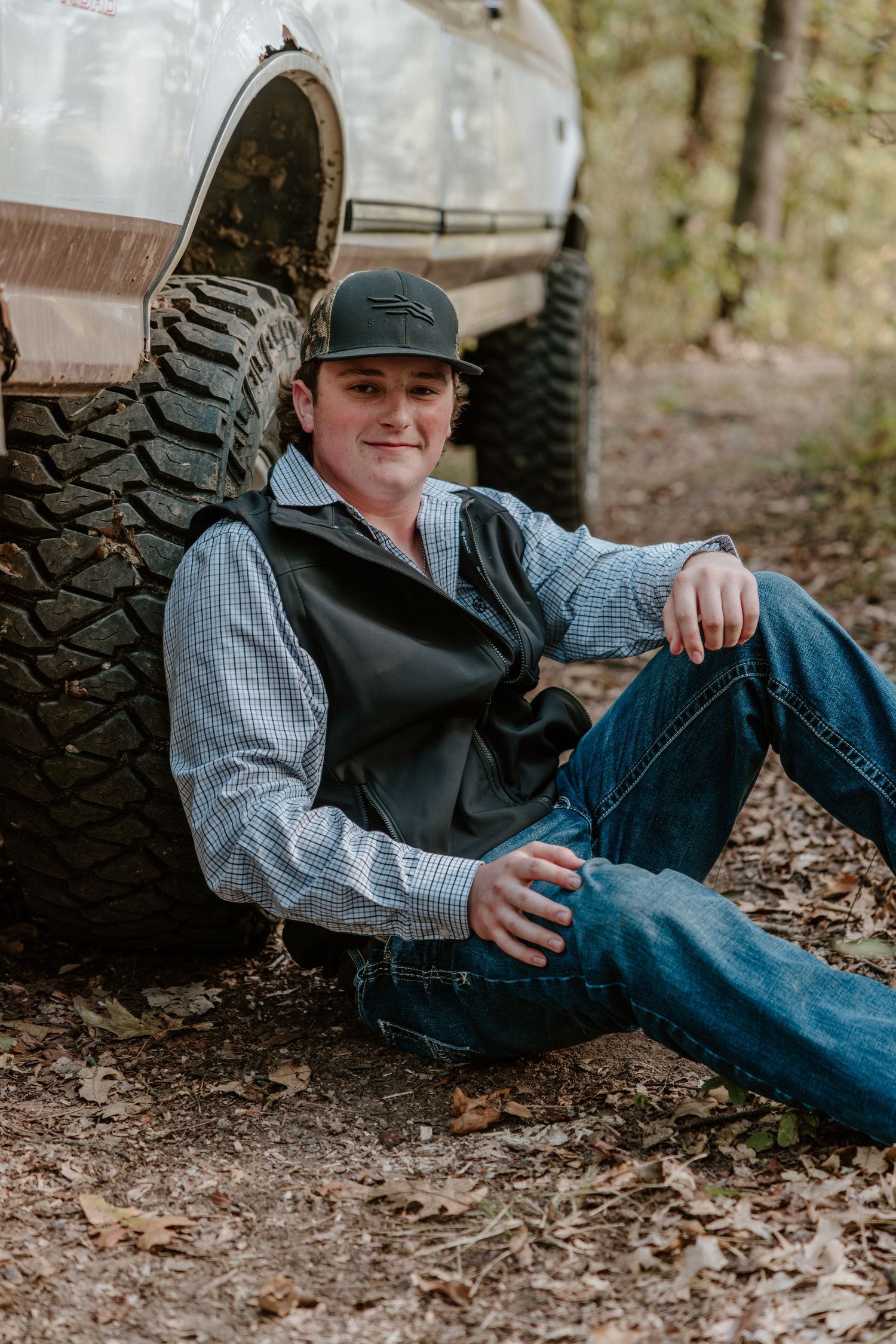 Casual outdoor portrait of someone in plaid shirt and baseball cap reclining against stone wall in autumn setting.