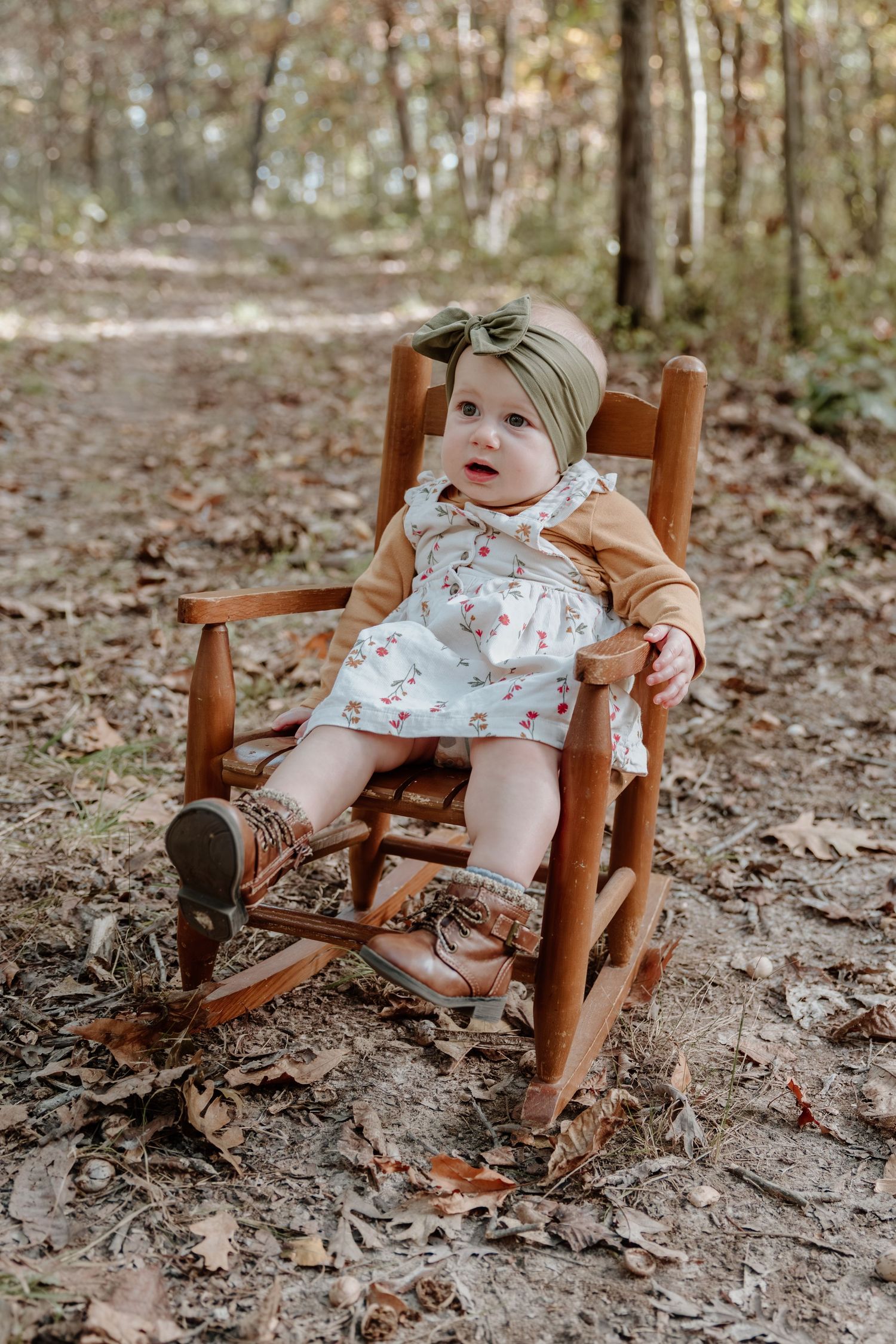 A small wooden rocking chair sits on a forest floor covered in fallen autumn leaves.