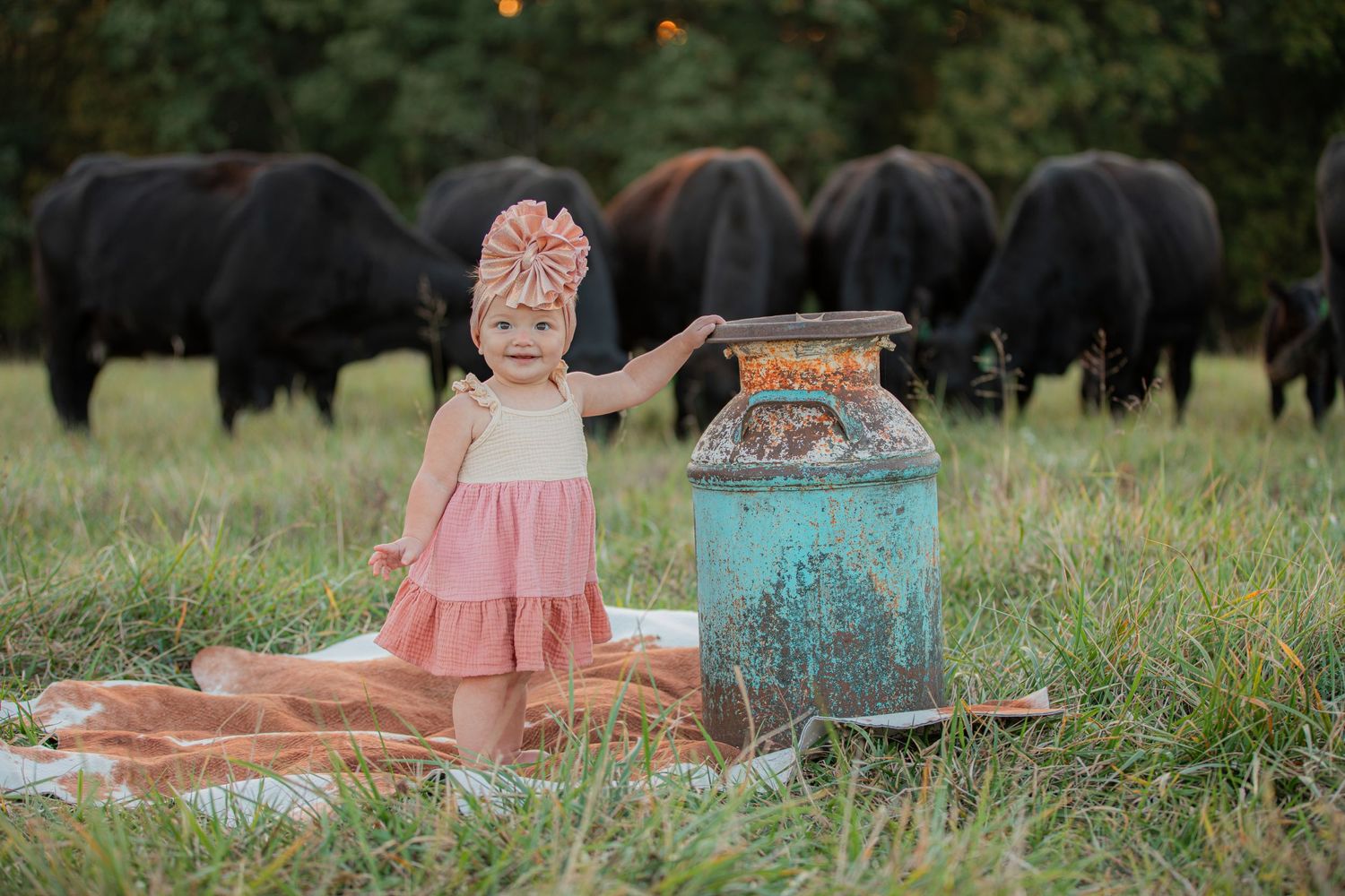 Small child in pink dress standing near vintage lantern with cattle grazing in field.