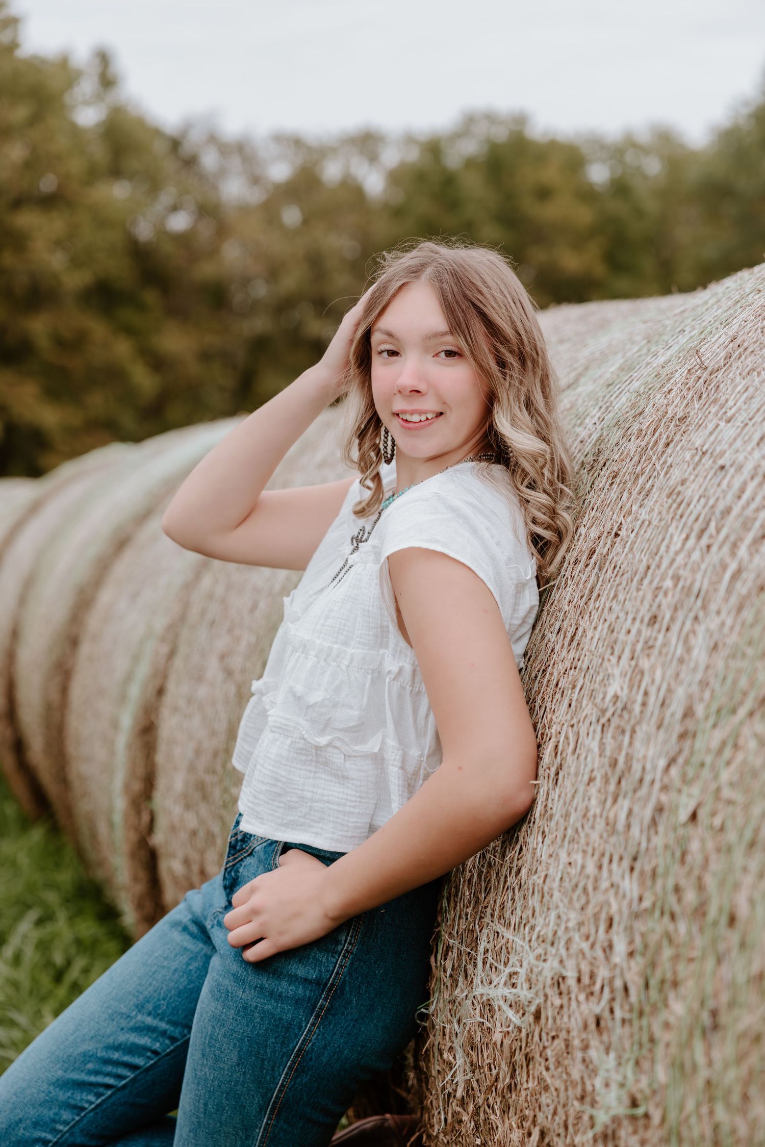 A series of outdoor portrait photos taken against round hay bales in a rural field setting.