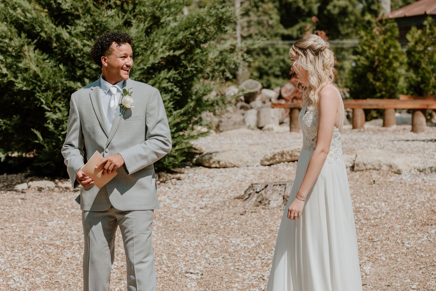 Groom in grey suit smiling at bride in strapless gown during outdoor first look.