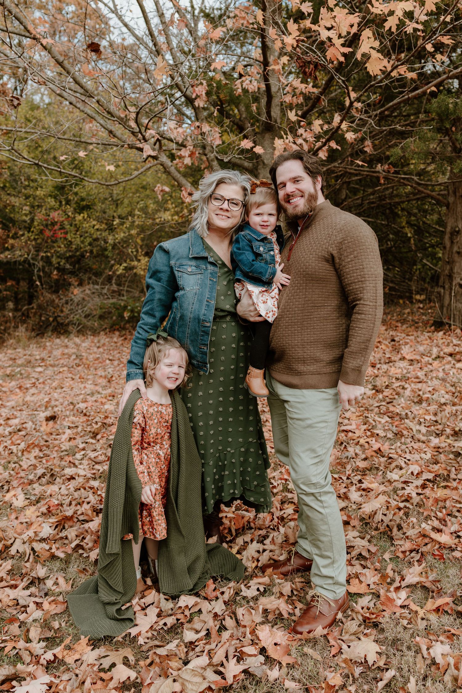 Group poses together in autumn forest setting surrounded by fallen leaves and bare trees.