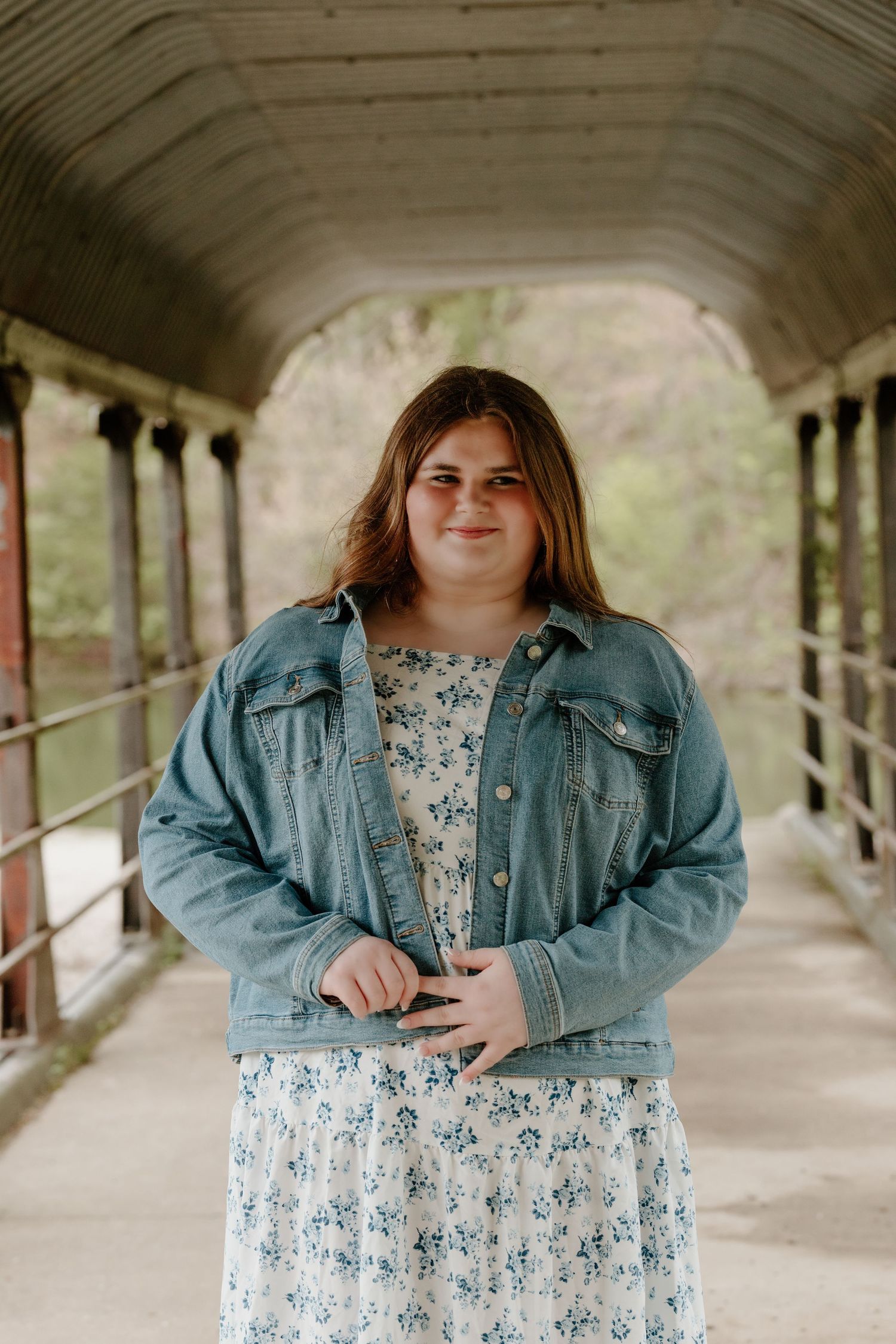 Standing in a covered walkway wearing a denim jacket and floral dress on a spring day.