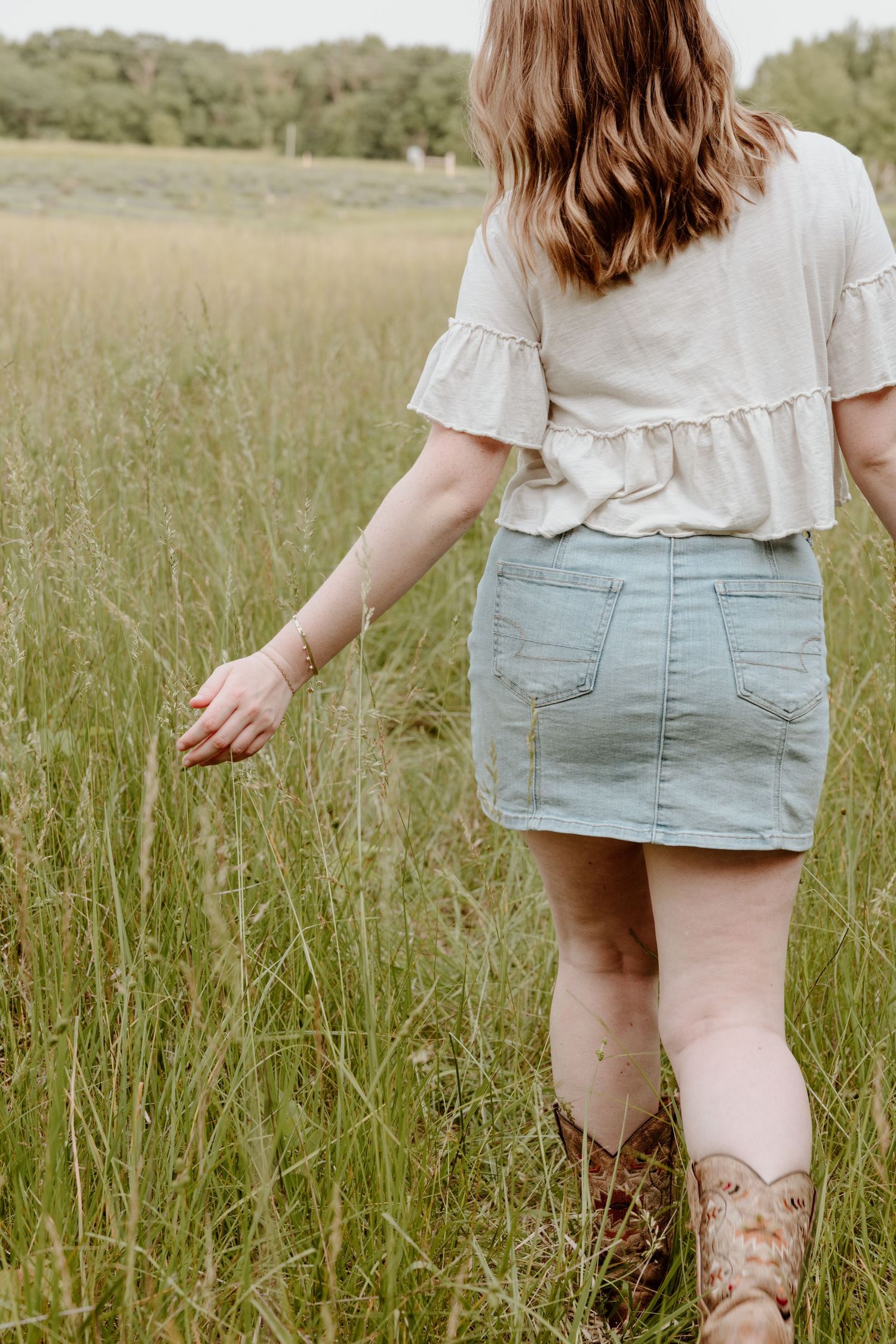A sequence of soft-focus images showing a person in a denim skirt walking through a serene summer meadow at dusk.
