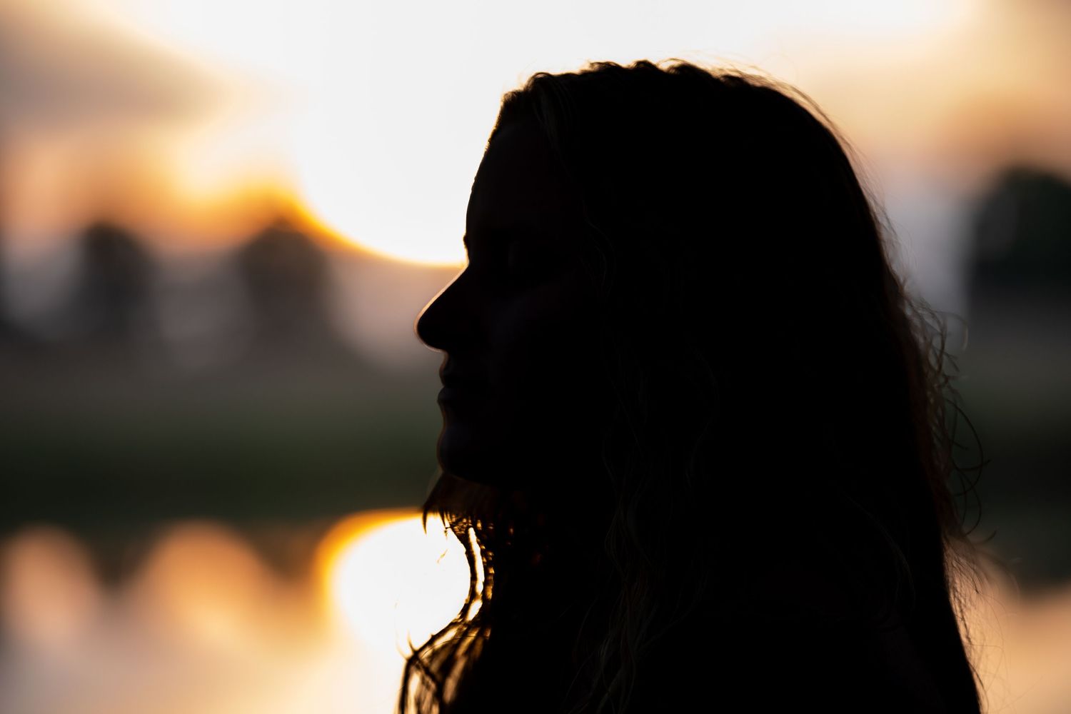 Silhouette of a person against sunset sky with water reflection.