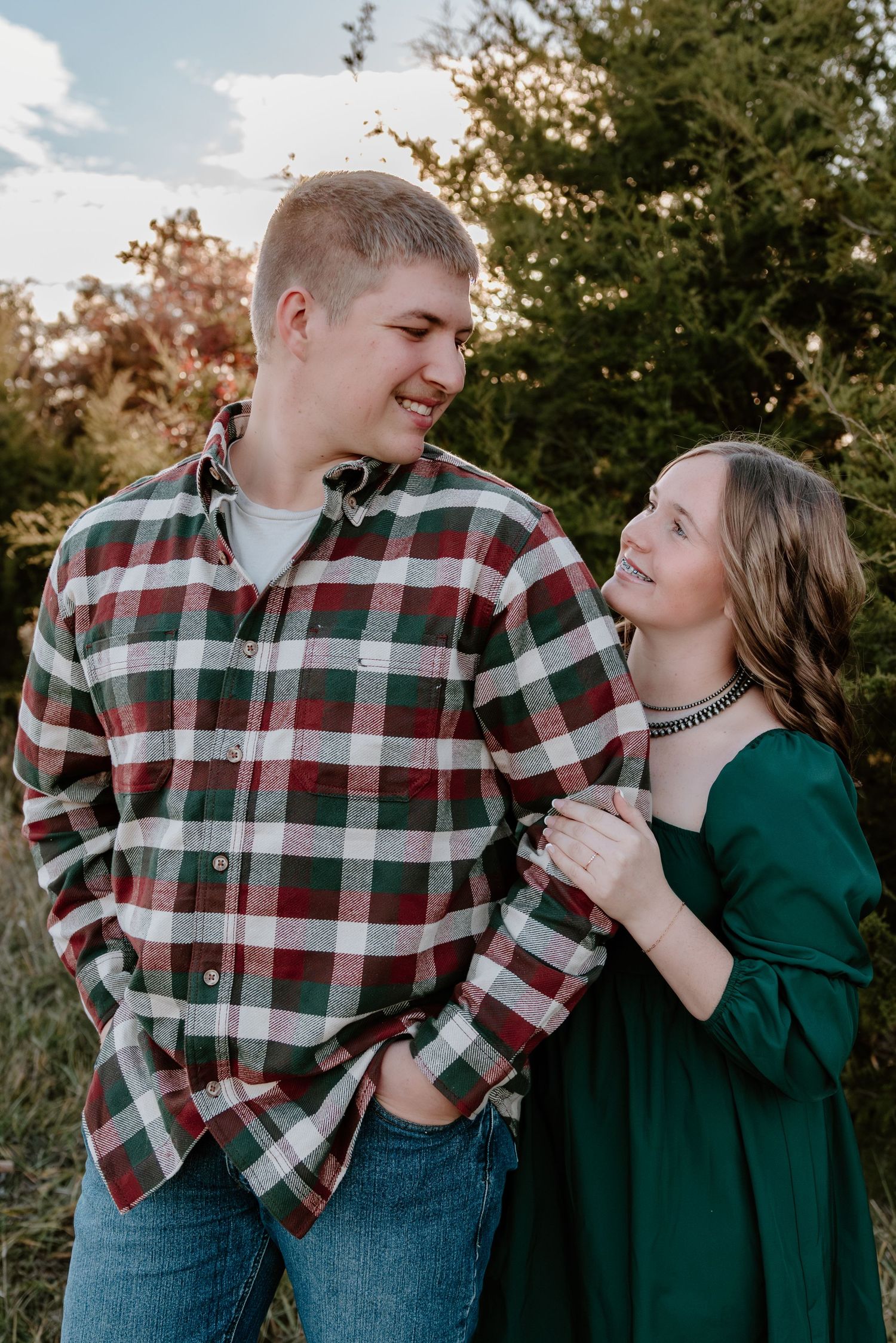 A couple shares a romantic moment outdoors, with one wearing a plaid flannel shirt and the other in an emerald green dress.