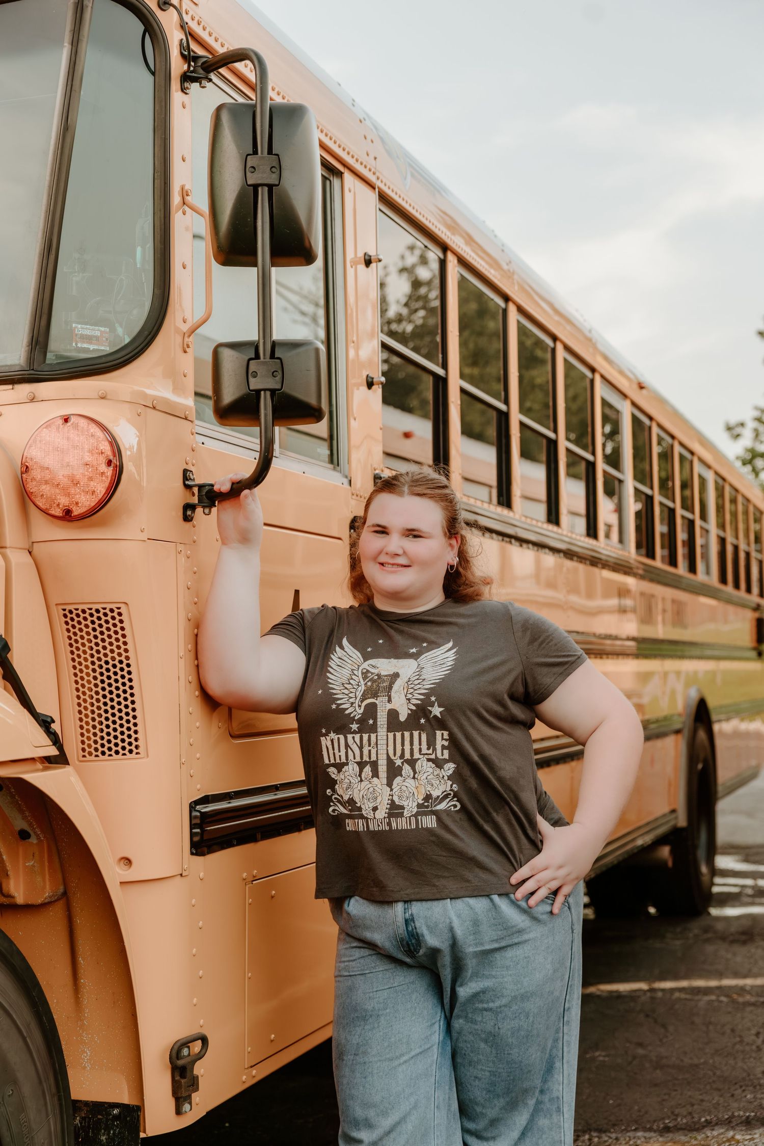Student in graphic t-shirt poses alongside a classic yellow school bus exterior.