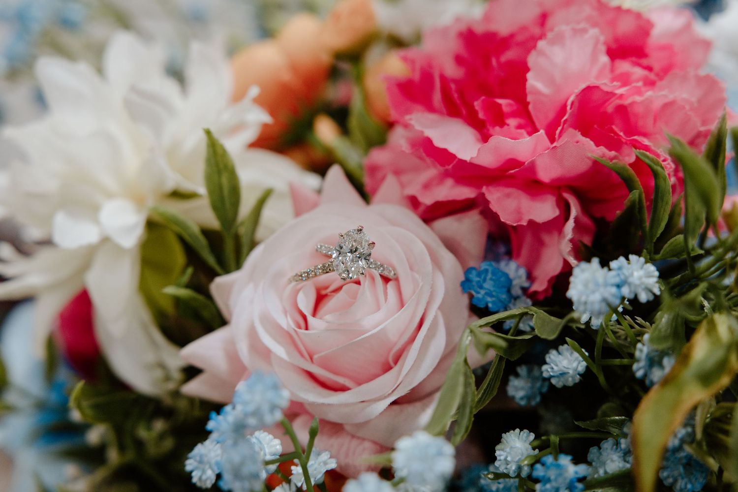 Diamond engagement ring nestled in a pink rose surrounded by colorful wedding bouquet flowers.