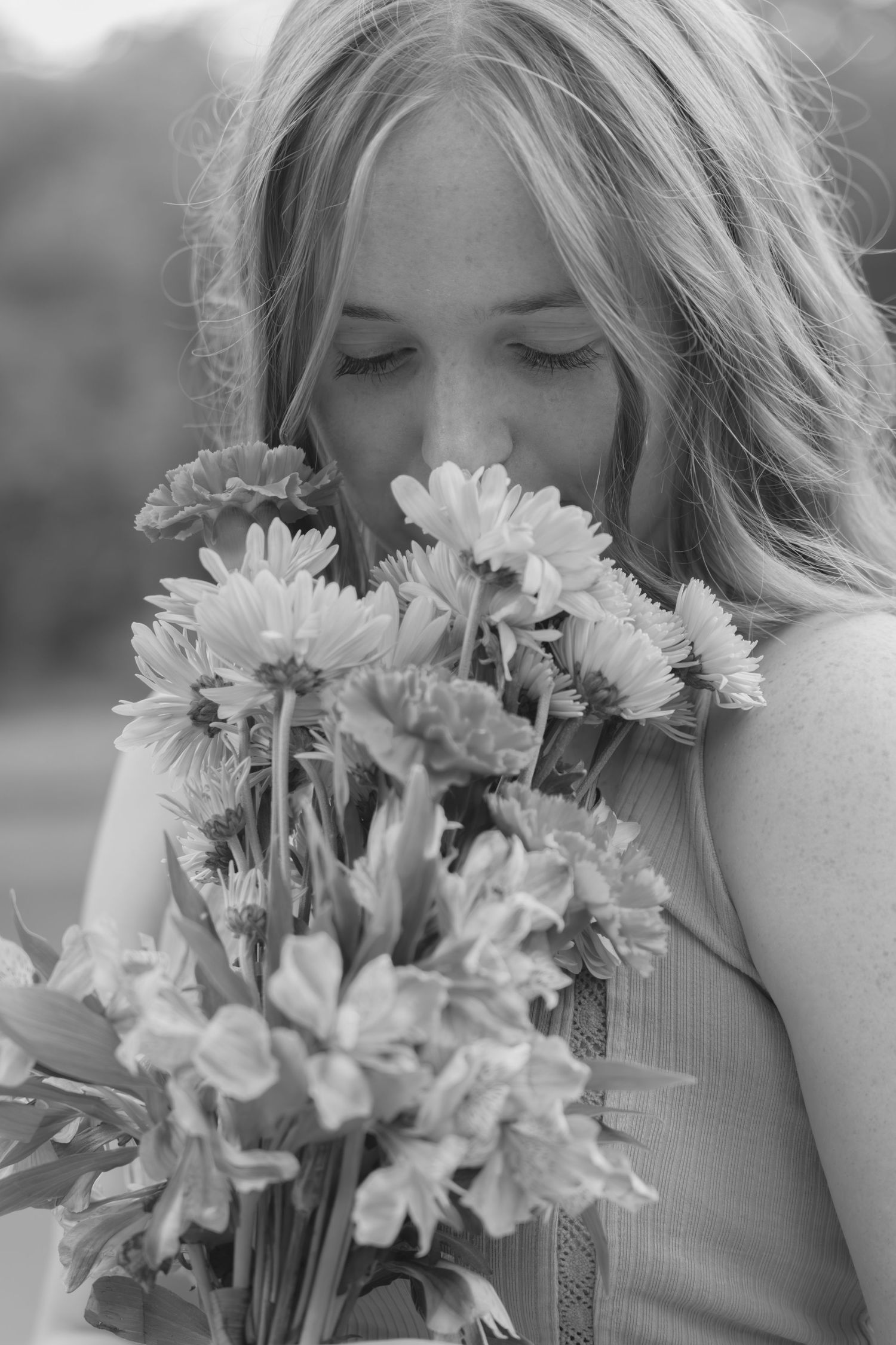 A black and white photo series shows someone holding and smelling a bouquet of fresh daisies in natural light.