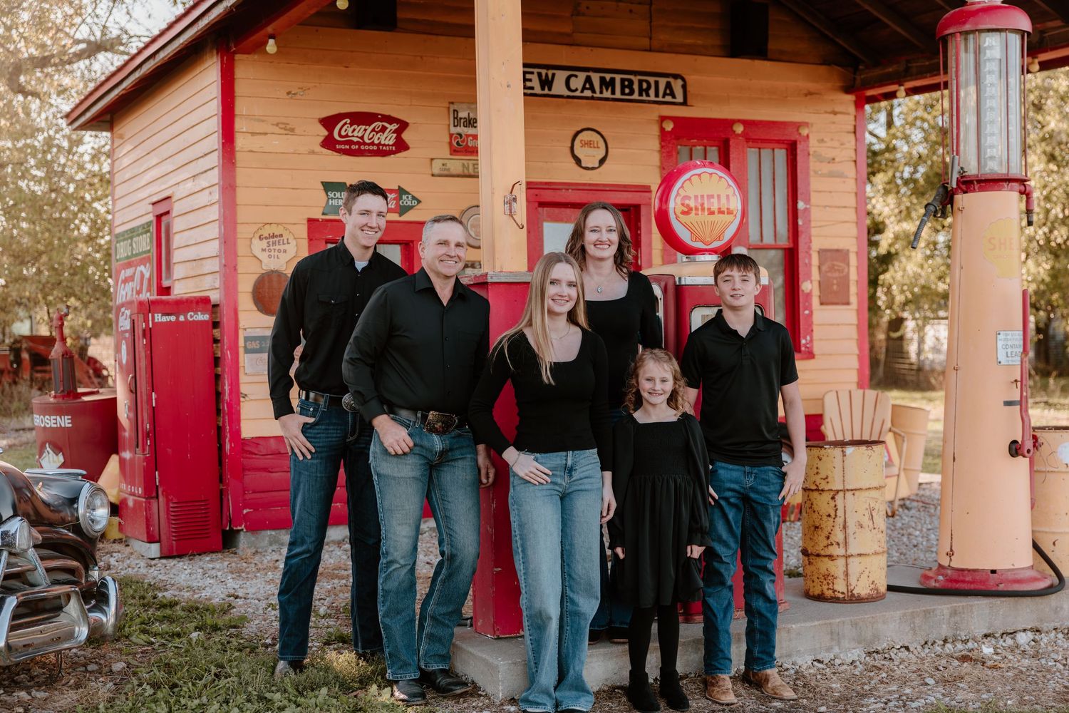 A group stands in front of a vintage pink gas station with antique Pepsi signs and retro gas pumps.