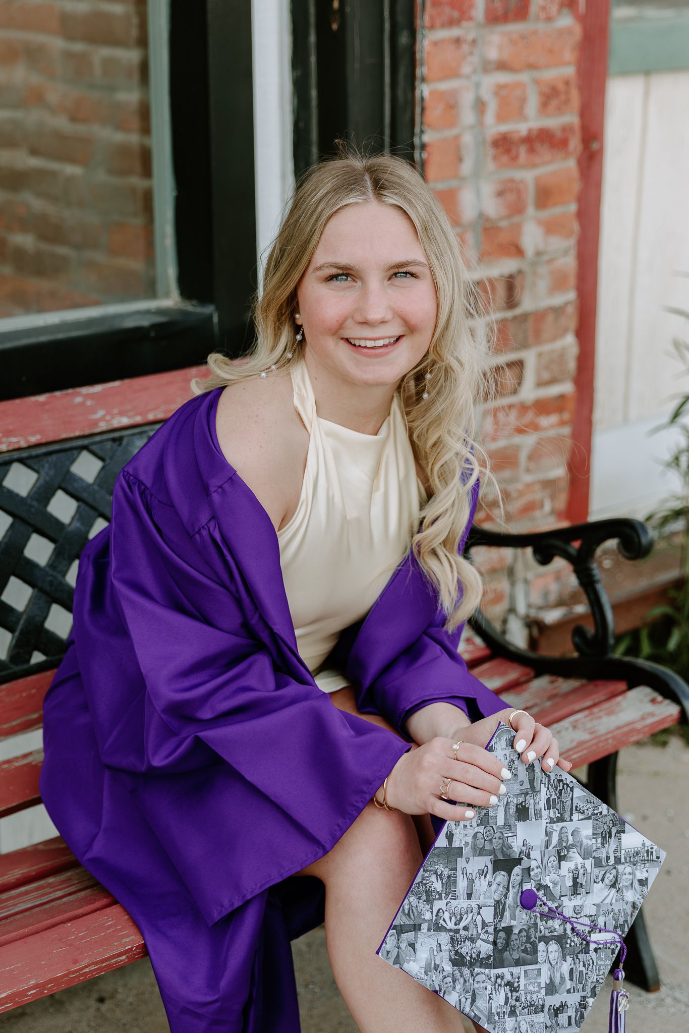 Smiling graduate in purple cap and gown sitting on a bench holding decorated mortarboard.