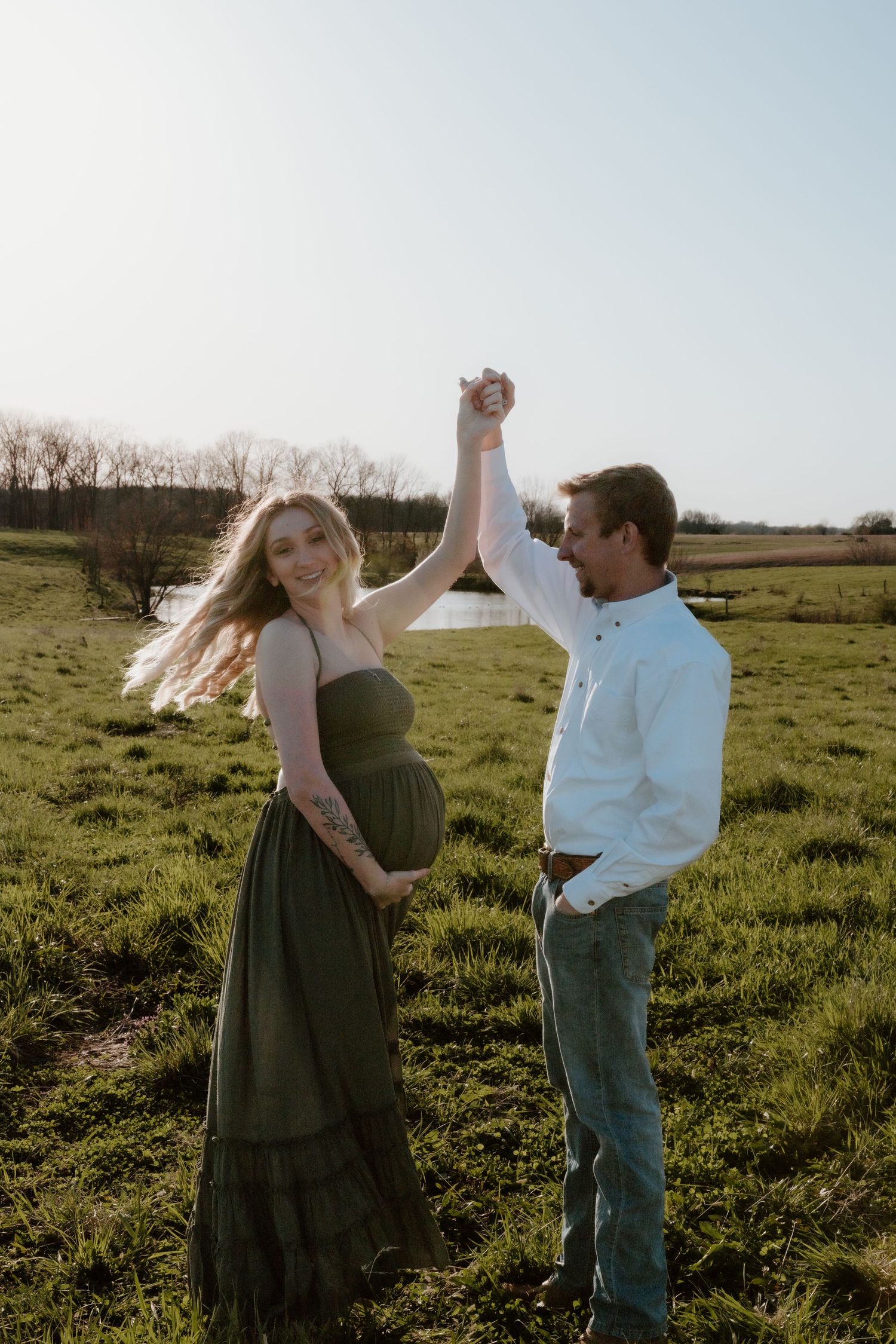 Couple dancing in a sunny meadow at sunset with the woman wearing a flowing olive green dress.