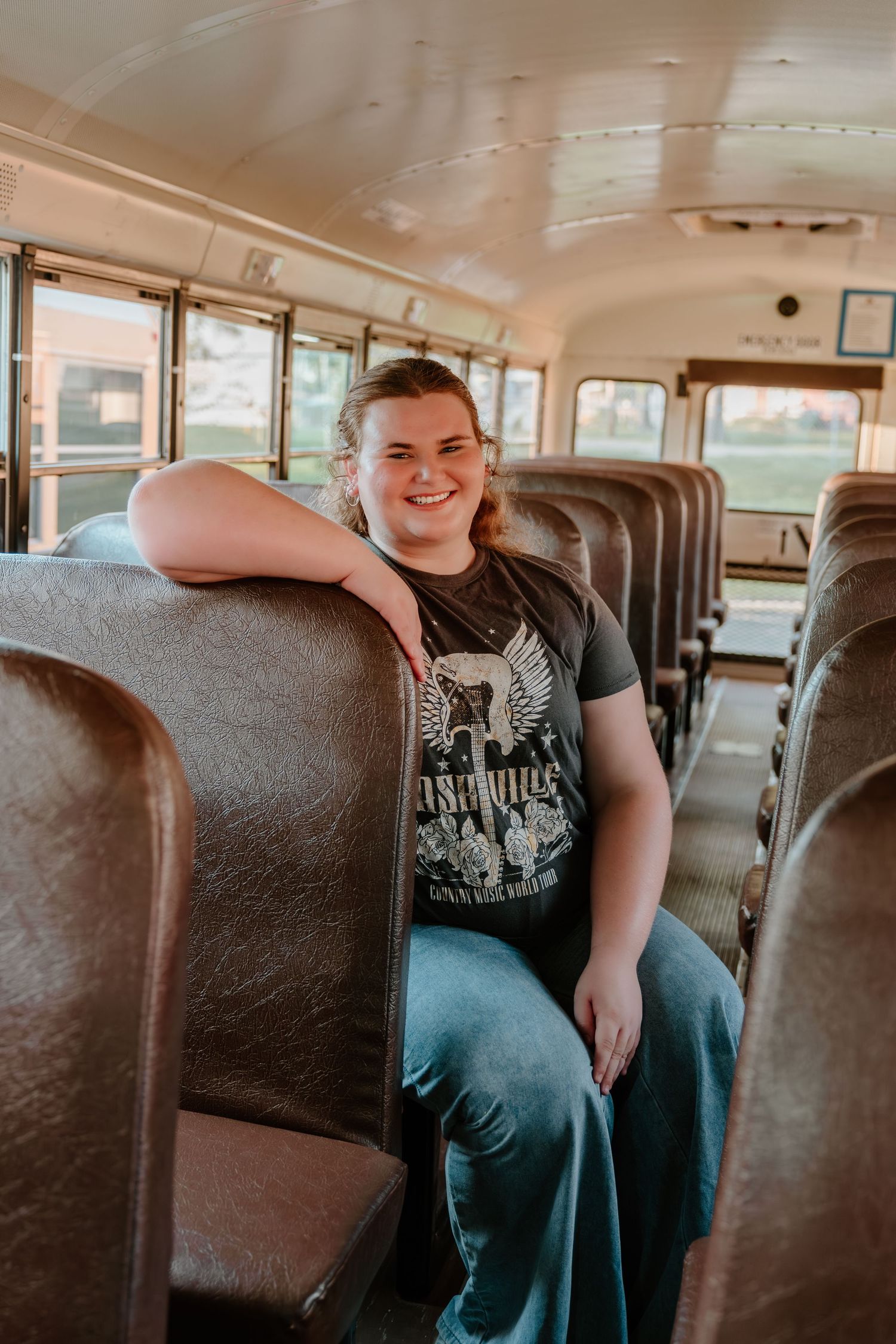 Student sits relaxed on brown leather seats inside a vintage school bus interior.